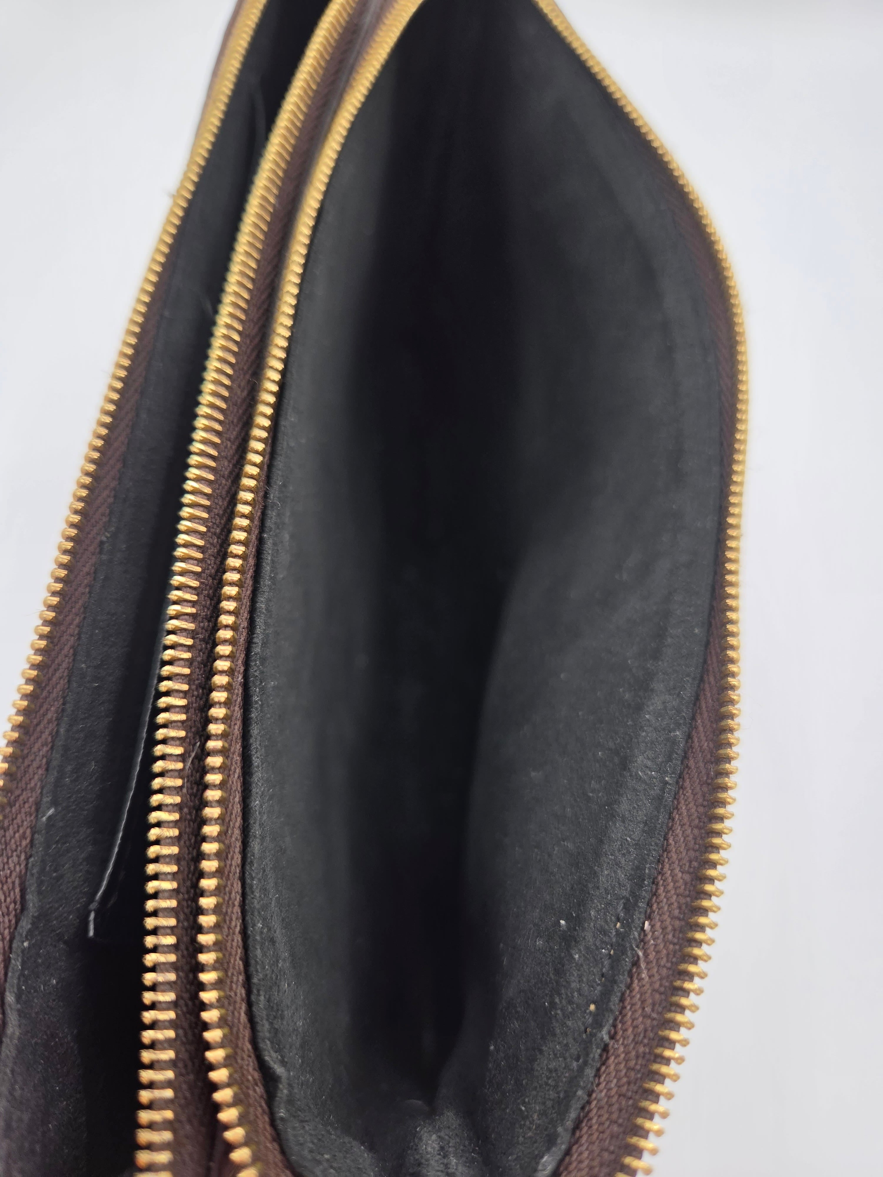 Open black leather pouch with gold zipper on a light gray background