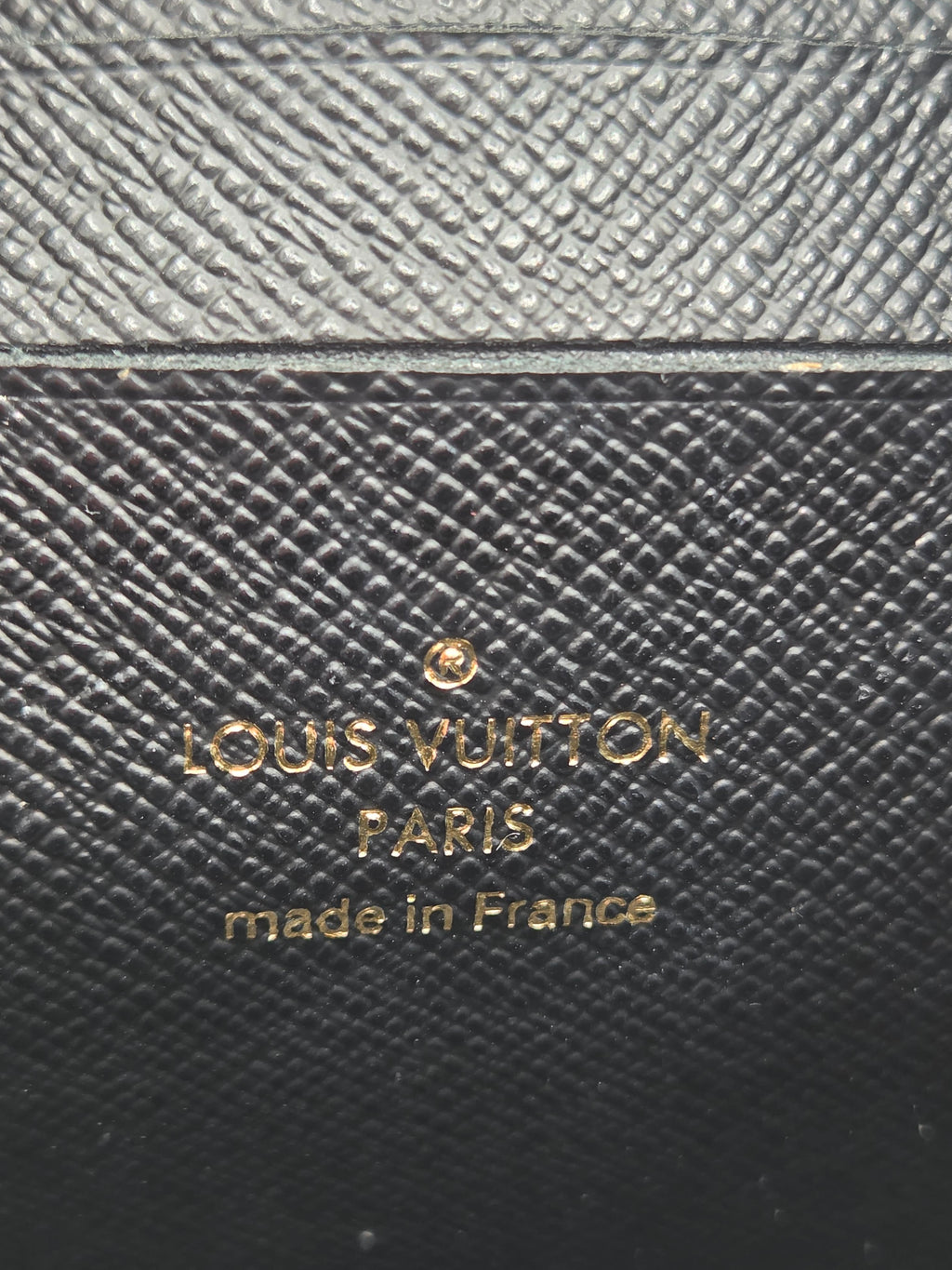 Louis Vuitton wallet with brand name and 'made in France' text on textured leather surface