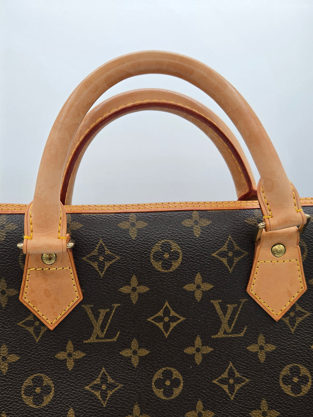 Louis Vuitton handbag with monogram pattern and tan handles on a light gray background