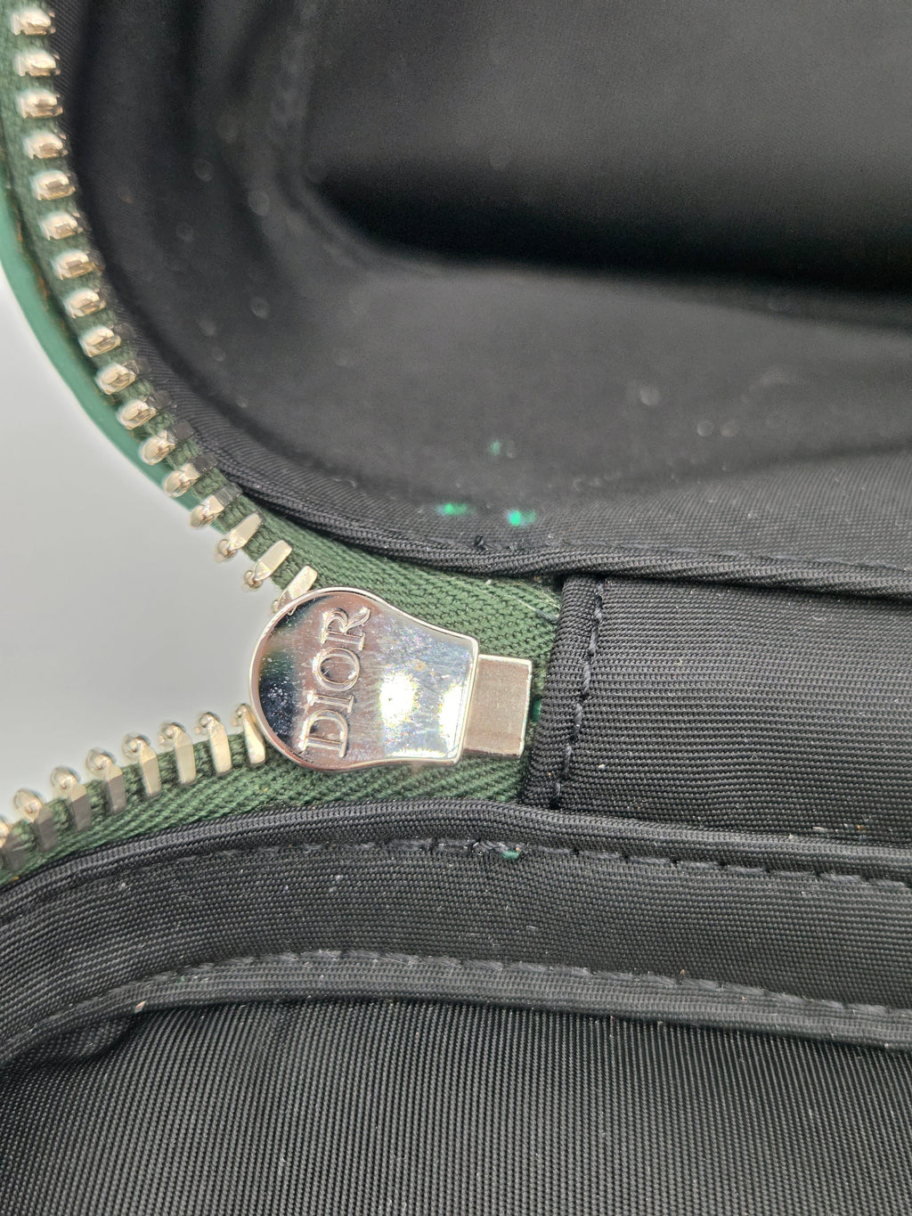 Close-up of a zipper with a 'Dior' tag on a black and green bag.