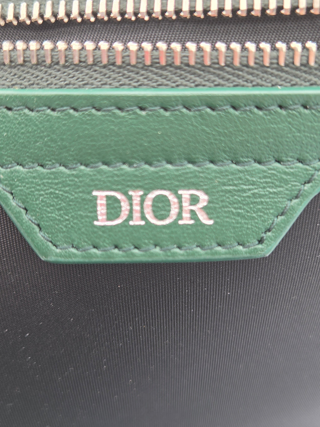 Close-up of a Dior logo on a green leather patch with a black background.