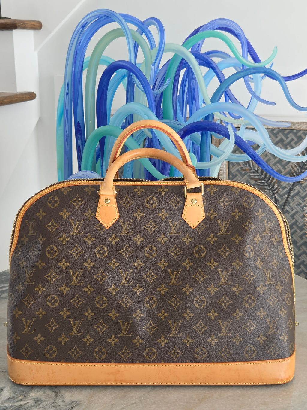 Designer handbag with monogram pattern on a stand against a neutral background