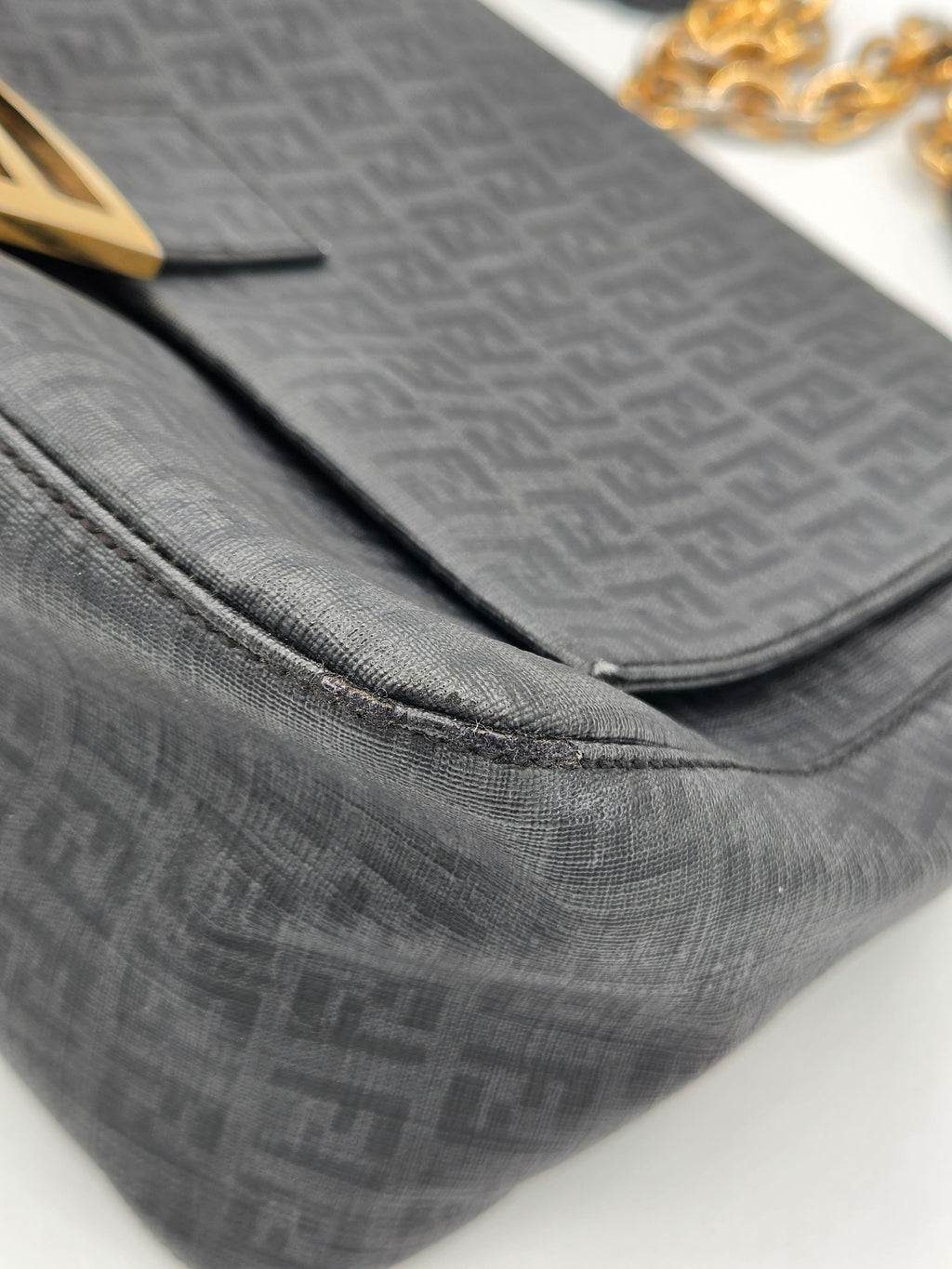 Close-up of a gray textured bag with a gold chain detail on a white background