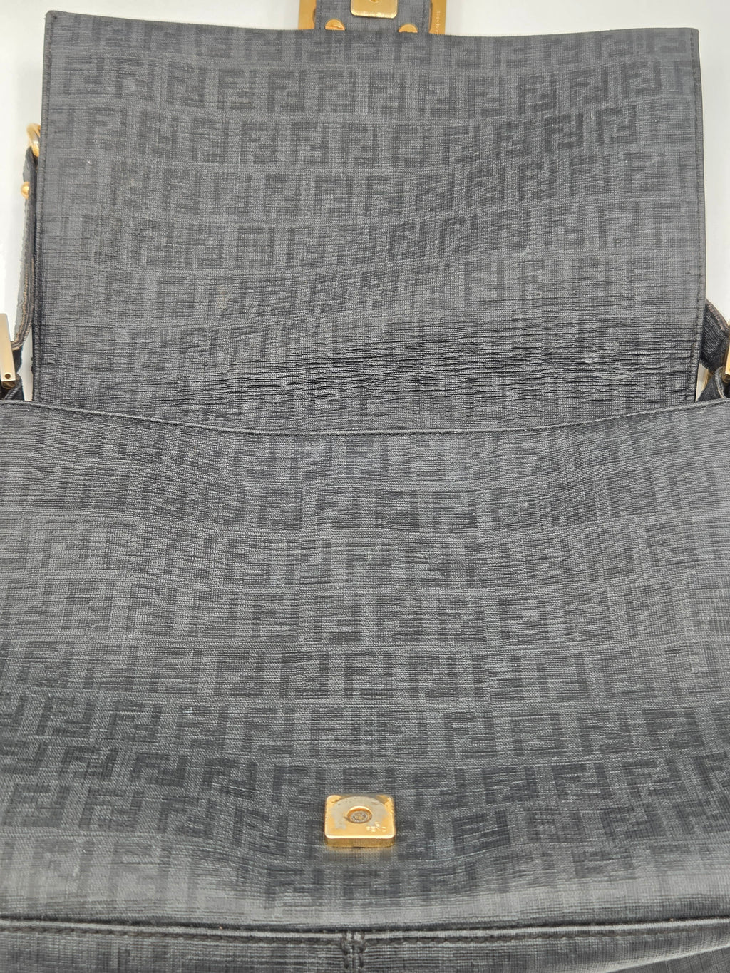 Close-up of a gray textured bag with a gold square emblem.