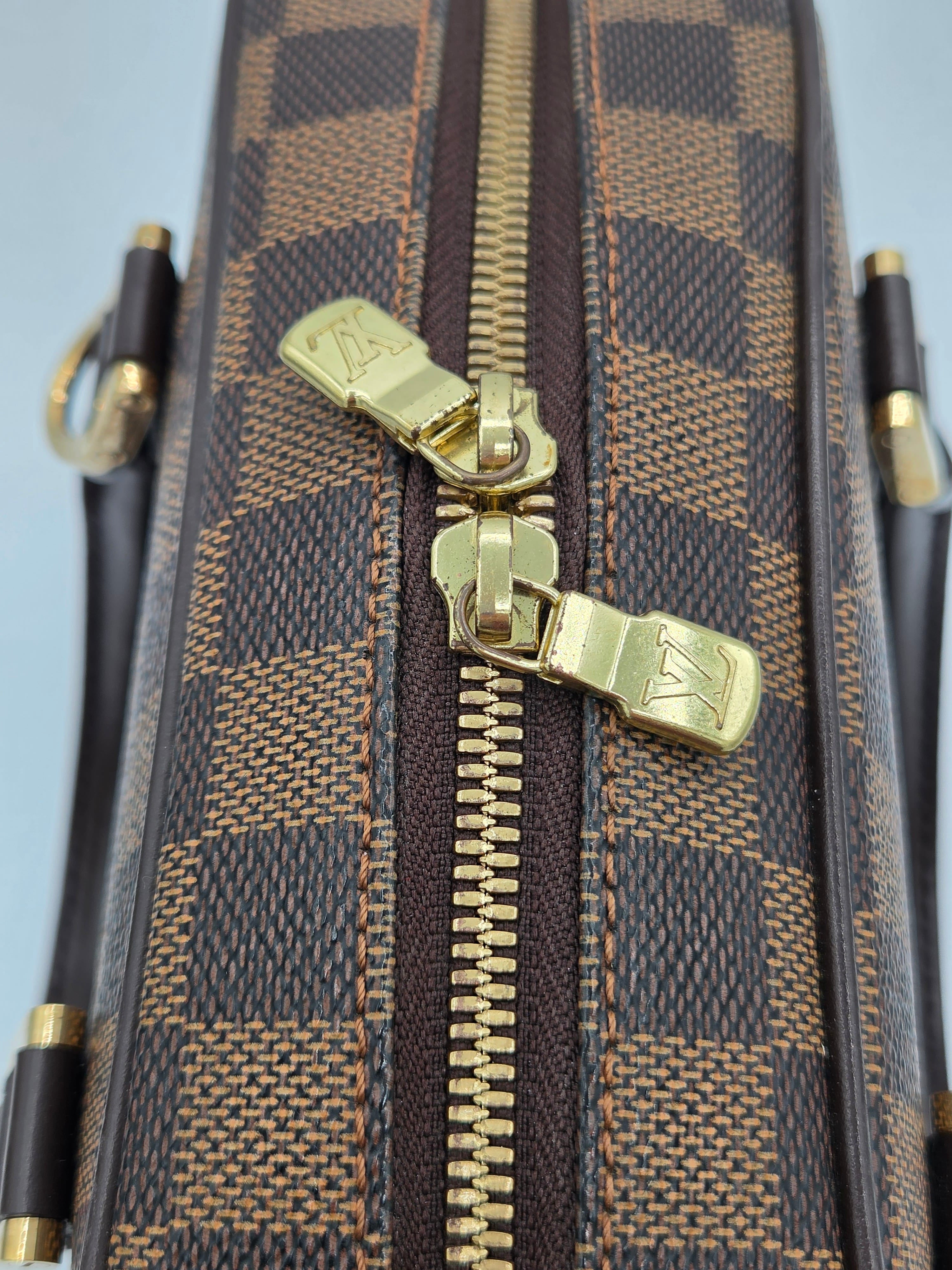 Close-up of a brown and gold patterned bag with a gold zipper, featuring a brand logo.