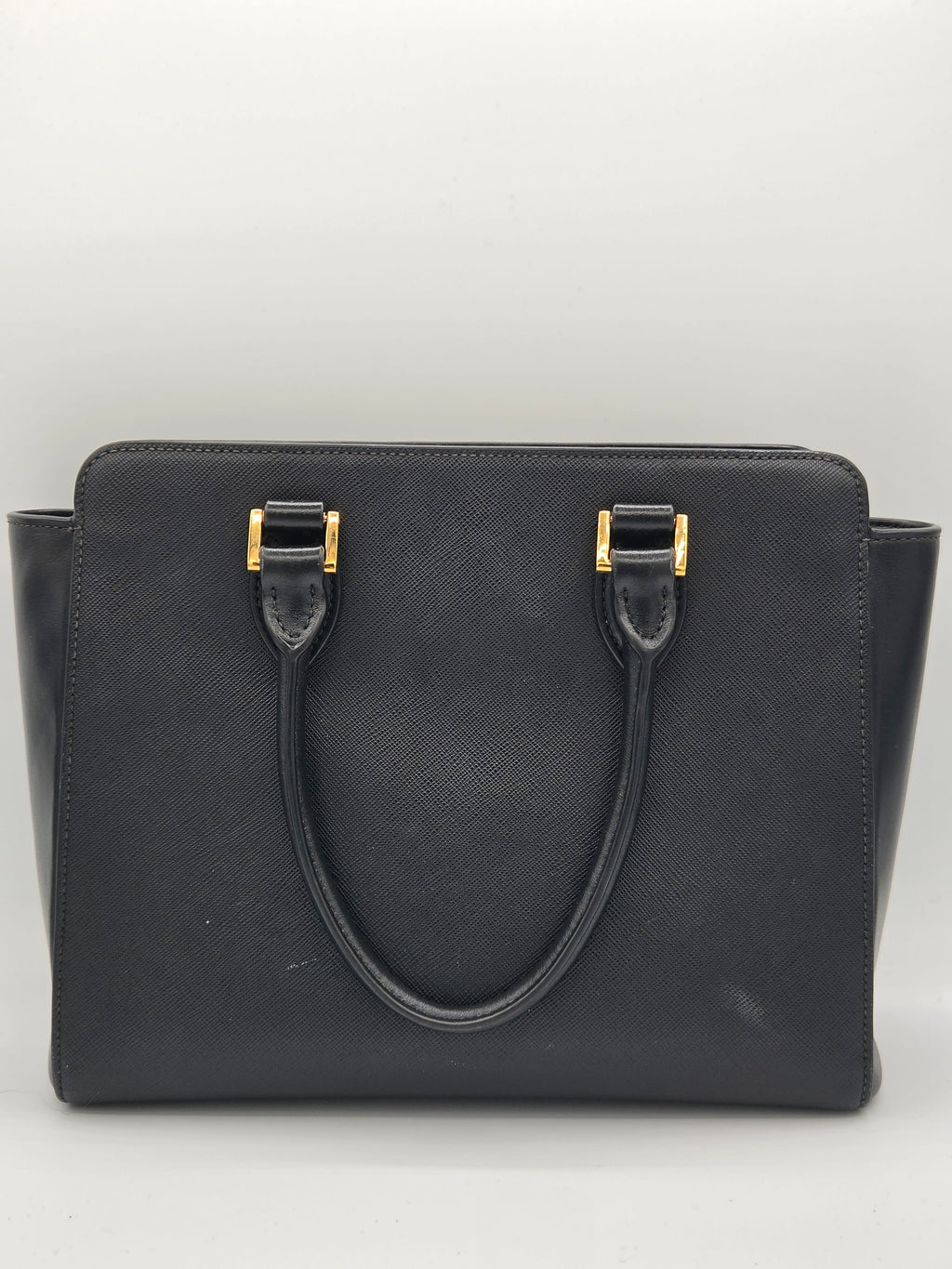 Black handbag with gold hardware on a light gray background