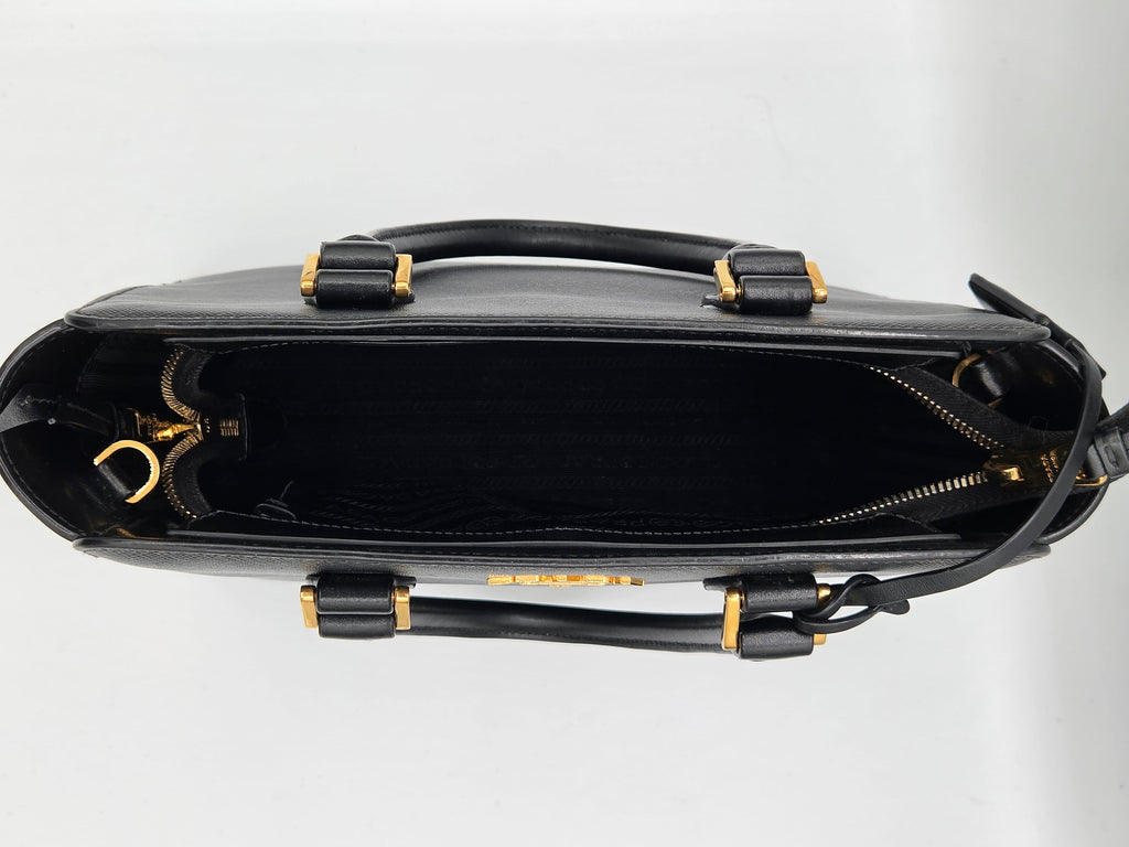 Black leather handbag with gold accents on a light gray background