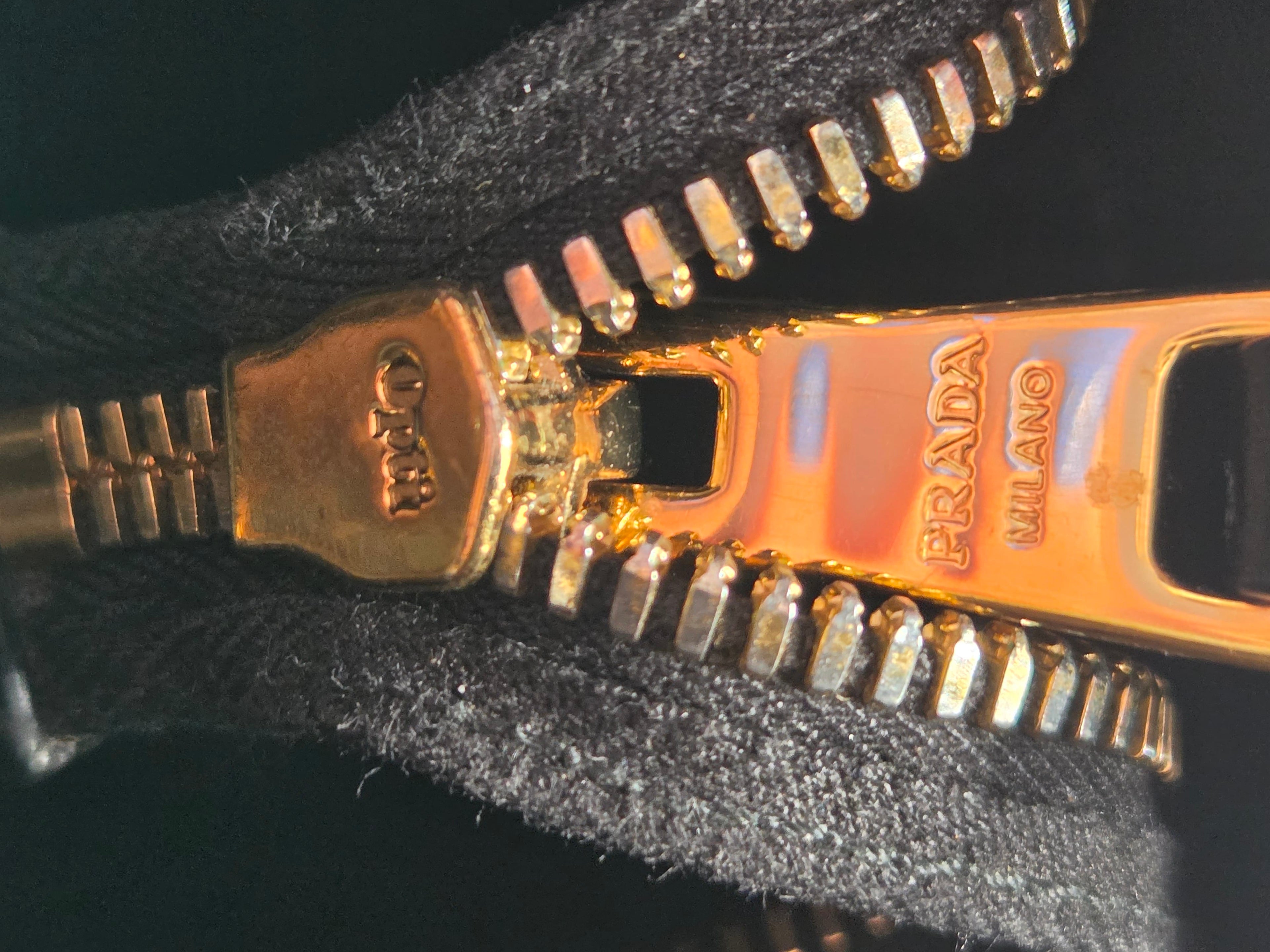 Gold Prada zipper on a black fabric background