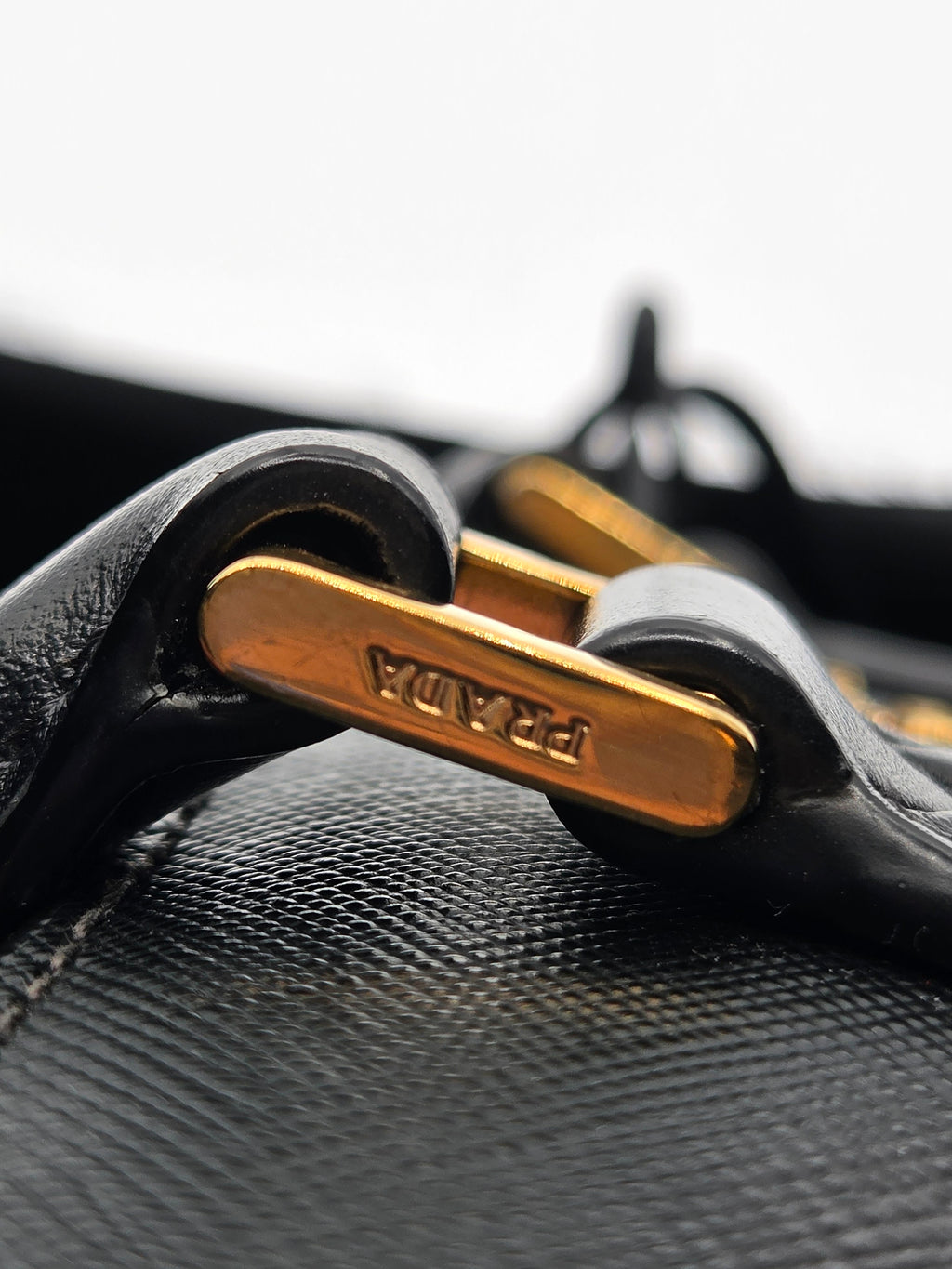 Close-up of a black leather bag with gold hardware featuring the brand name.