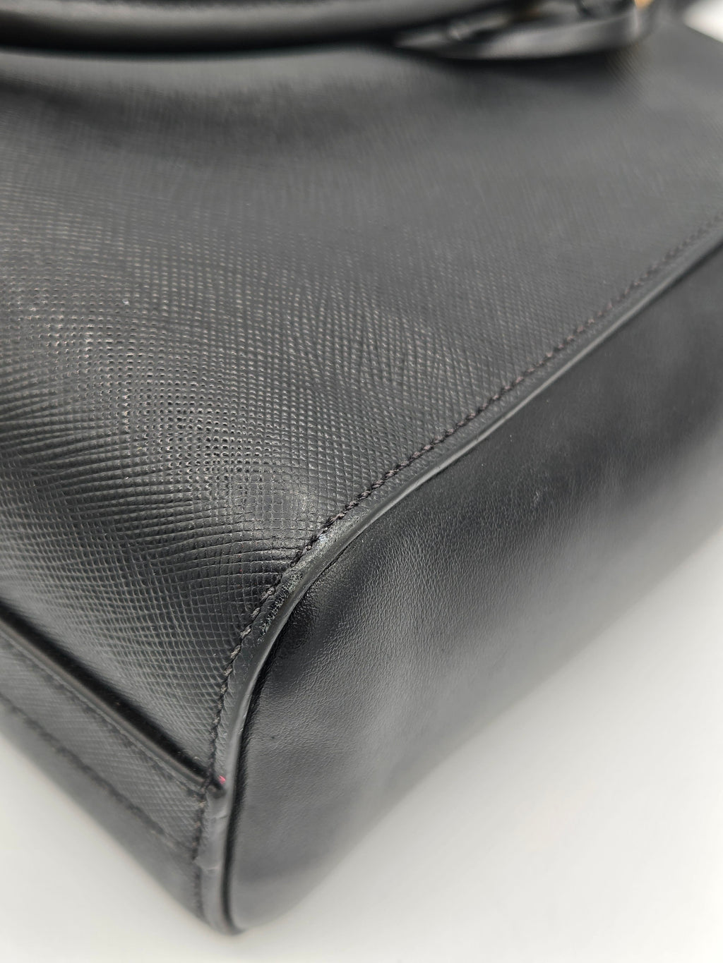 Close-up of a textured black leather bag corner on a light gray background