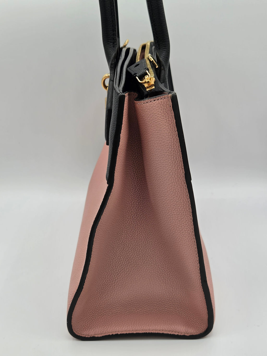 Close-up of a pink handbag with black trim on a light gray background