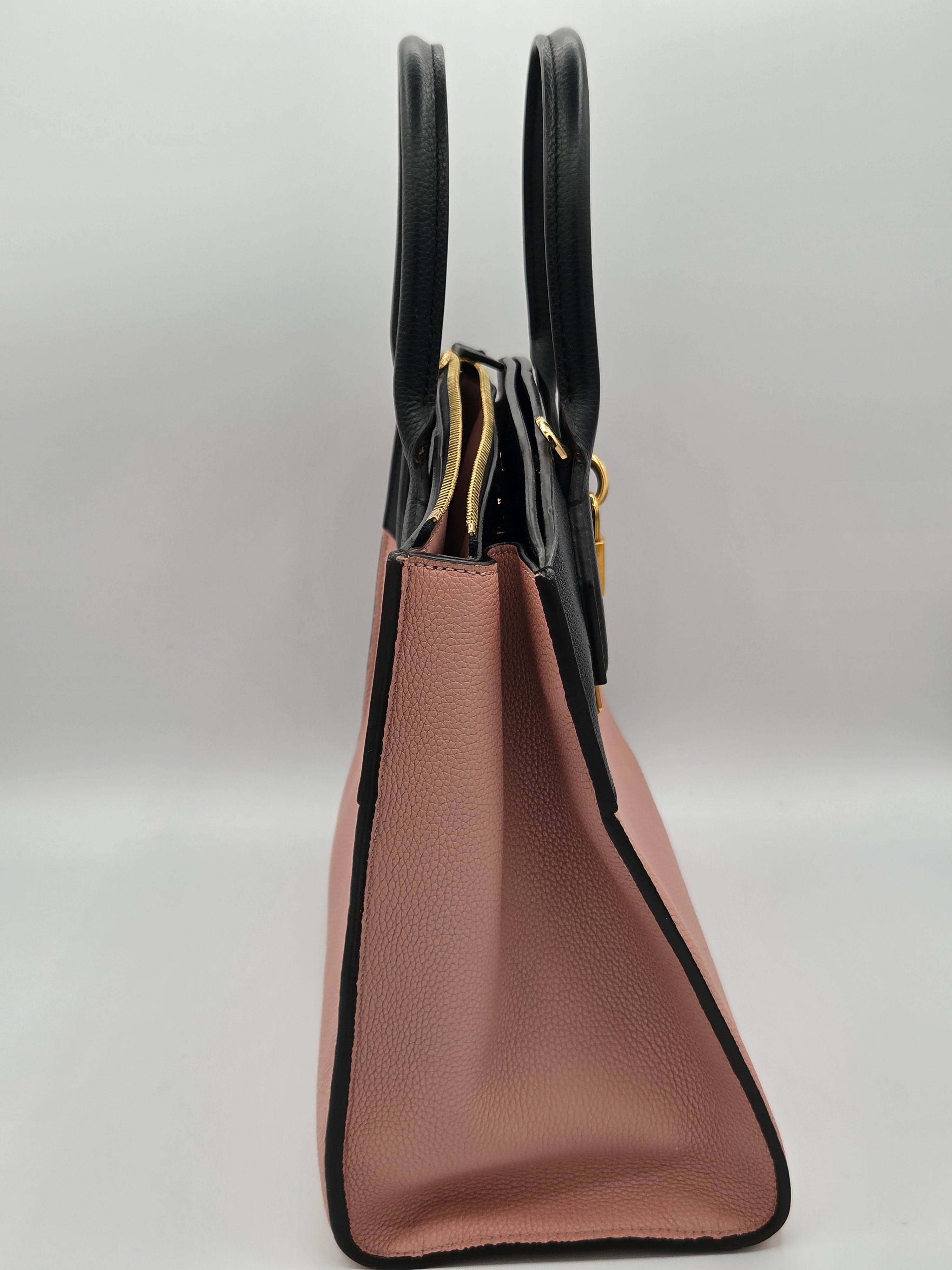 Pink handbag with black handles and trim on a light gray background