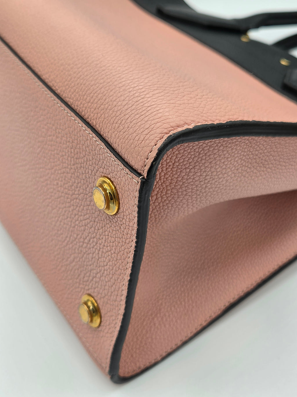 Close-up of a pink leather handbag with gold rivets on a light gray background