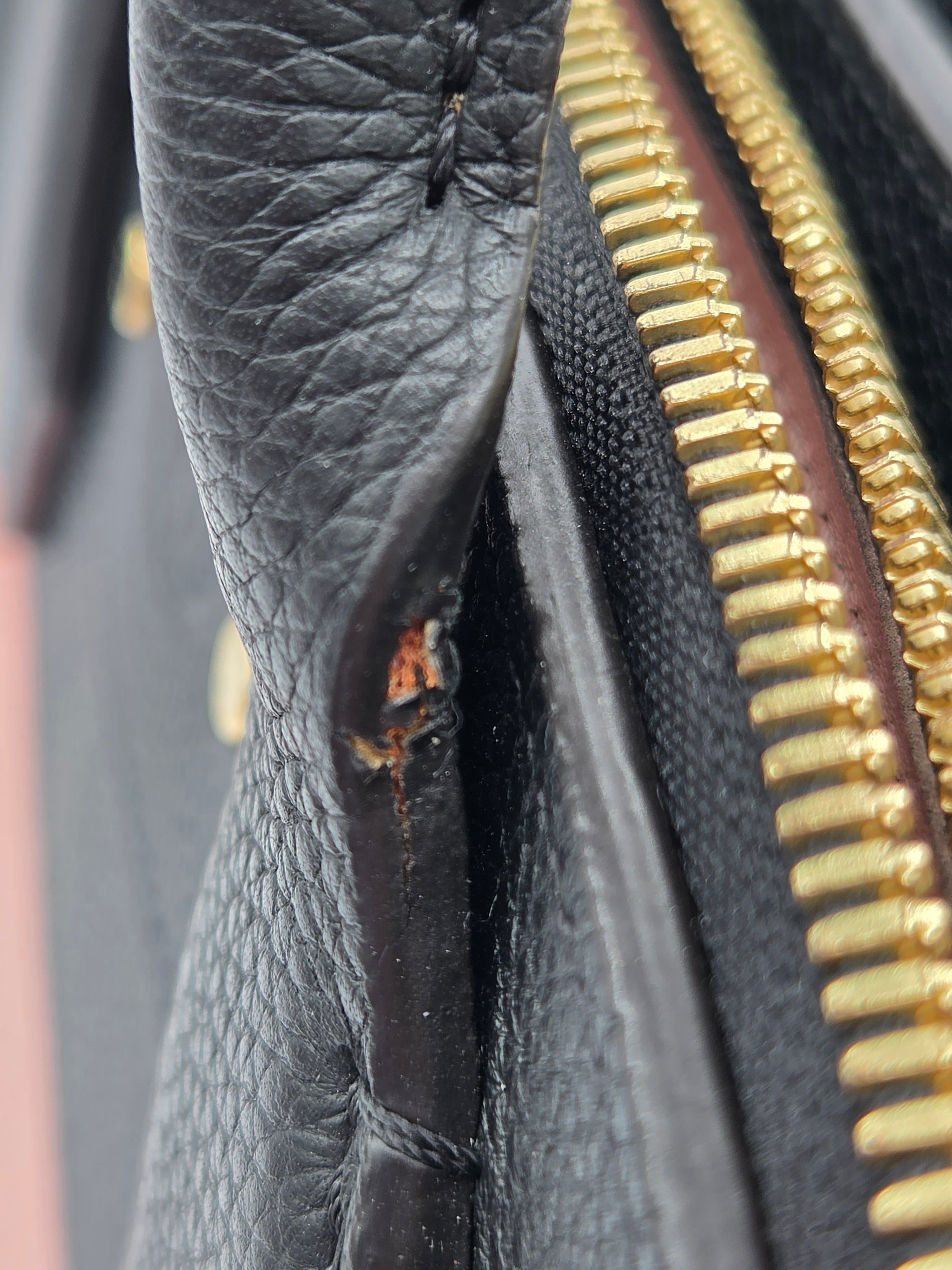 Close-up of a black leather bag with a gold zipper showing signs of wear.