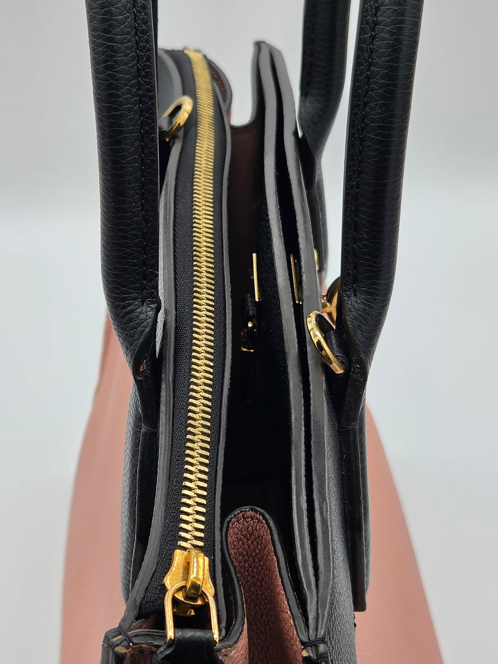 Close-up of a black handbag with gold zippers on a light gray background