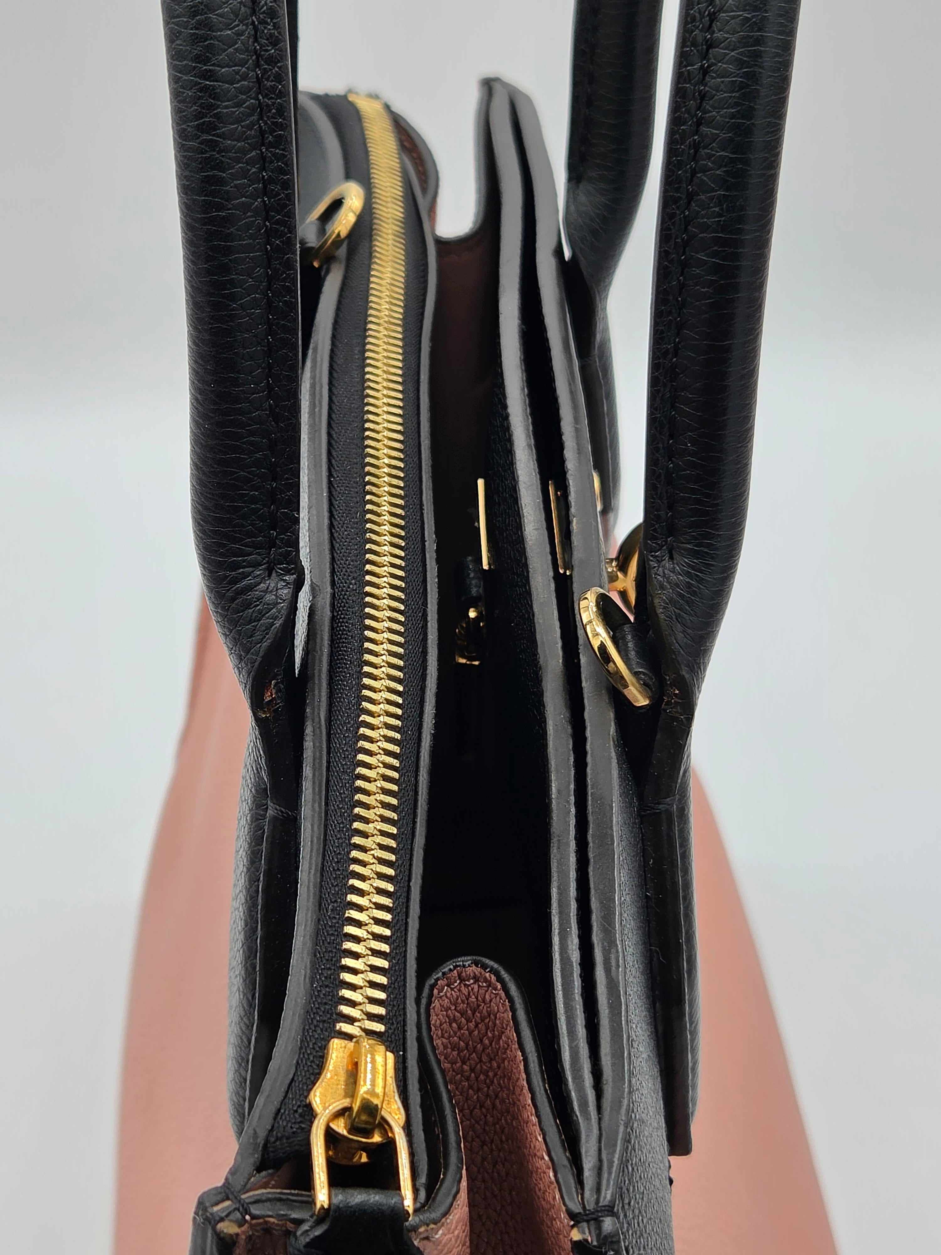Close-up of a black handbag with gold zippers on a light gray background