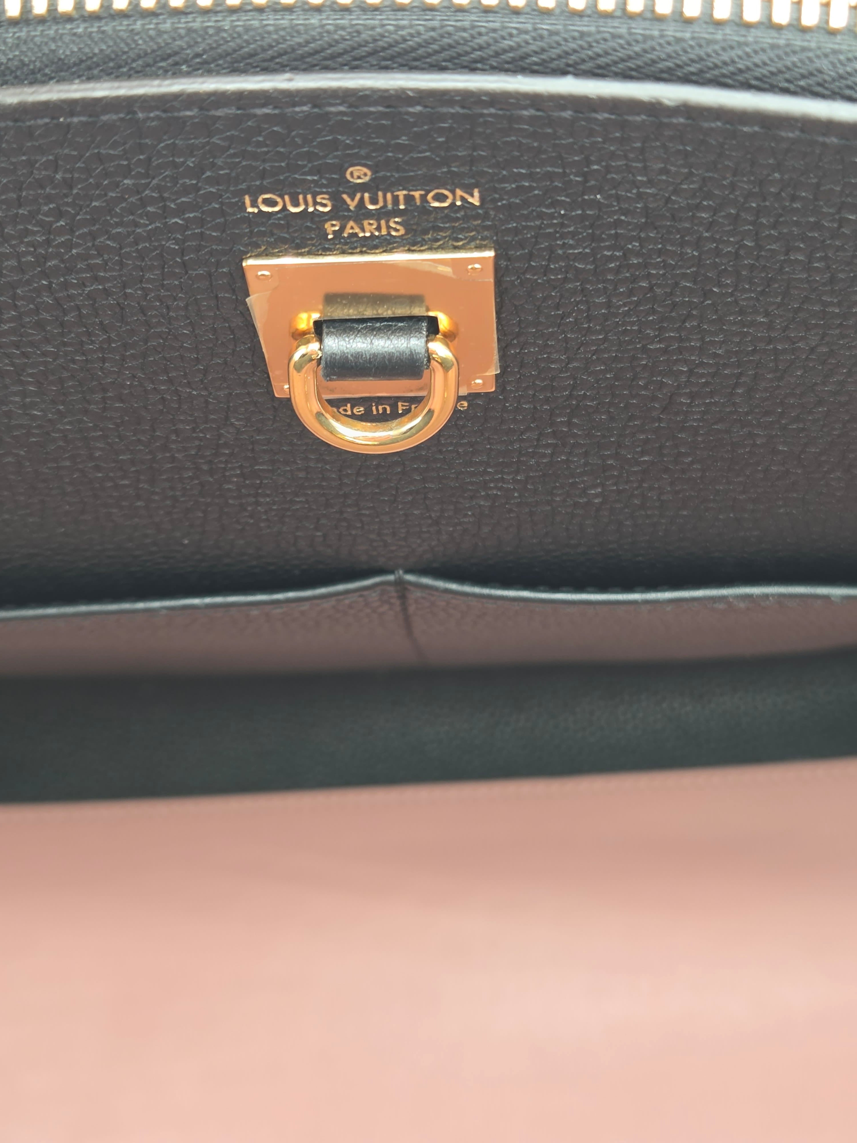 Close-up of a Louis Vuitton lock on a black leather bag with a pink background.