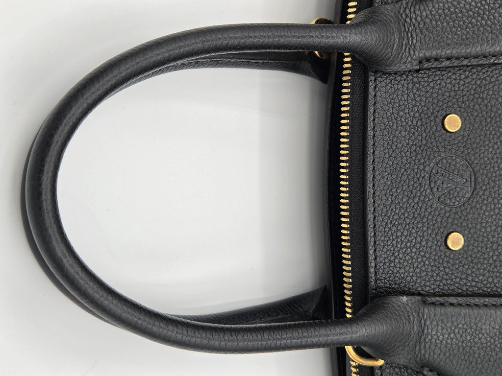 Close-up of a black leather handbag handle with gold accents on a white background