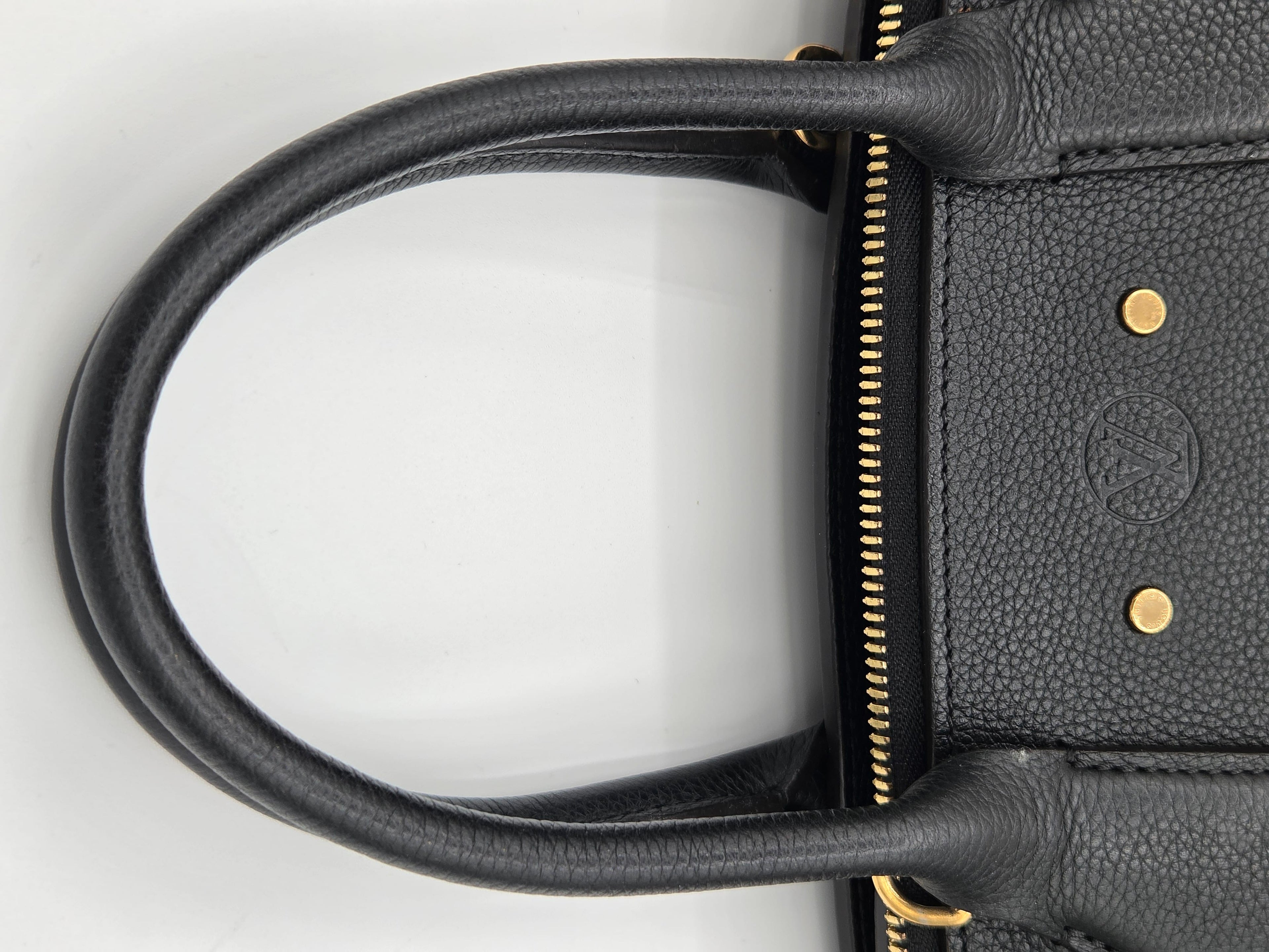 Close-up of a black leather handbag handle with gold accents on a white background