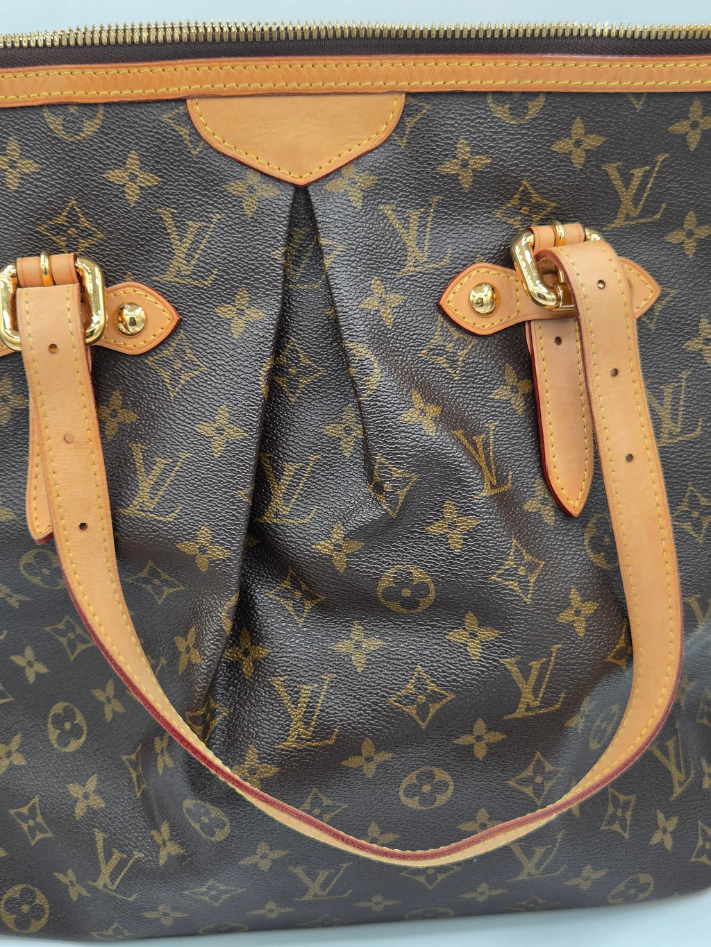 Louis Vuitton monogram handbag with tan leather handle and strap on a light blue background