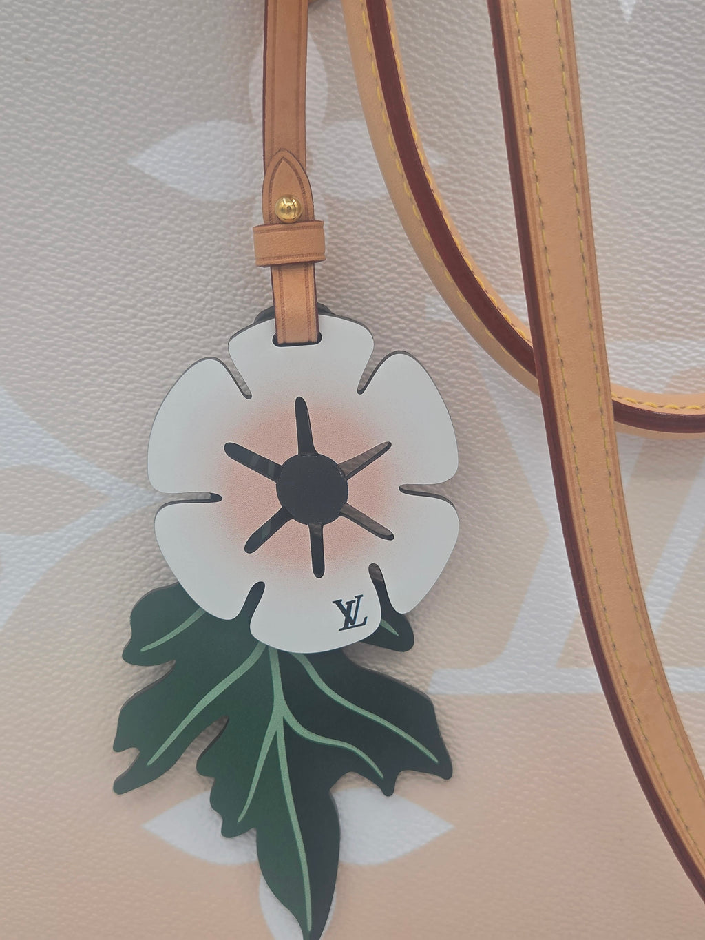 Floral-shaped bag charm with a brand logo on a beige background