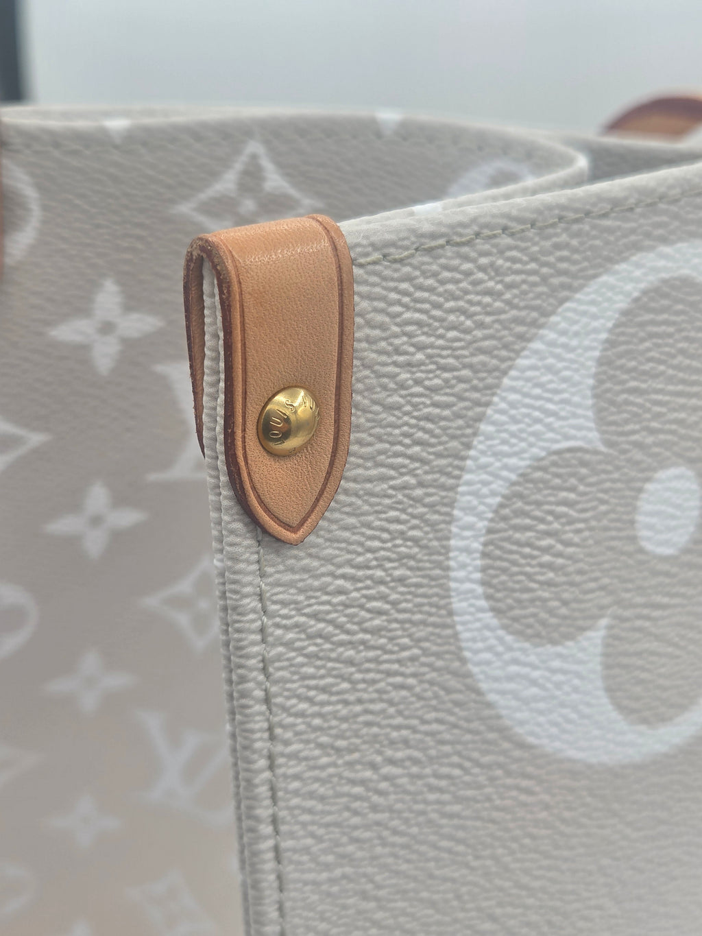 Close-up of a gray handbag with a brown leather strap and gold button.