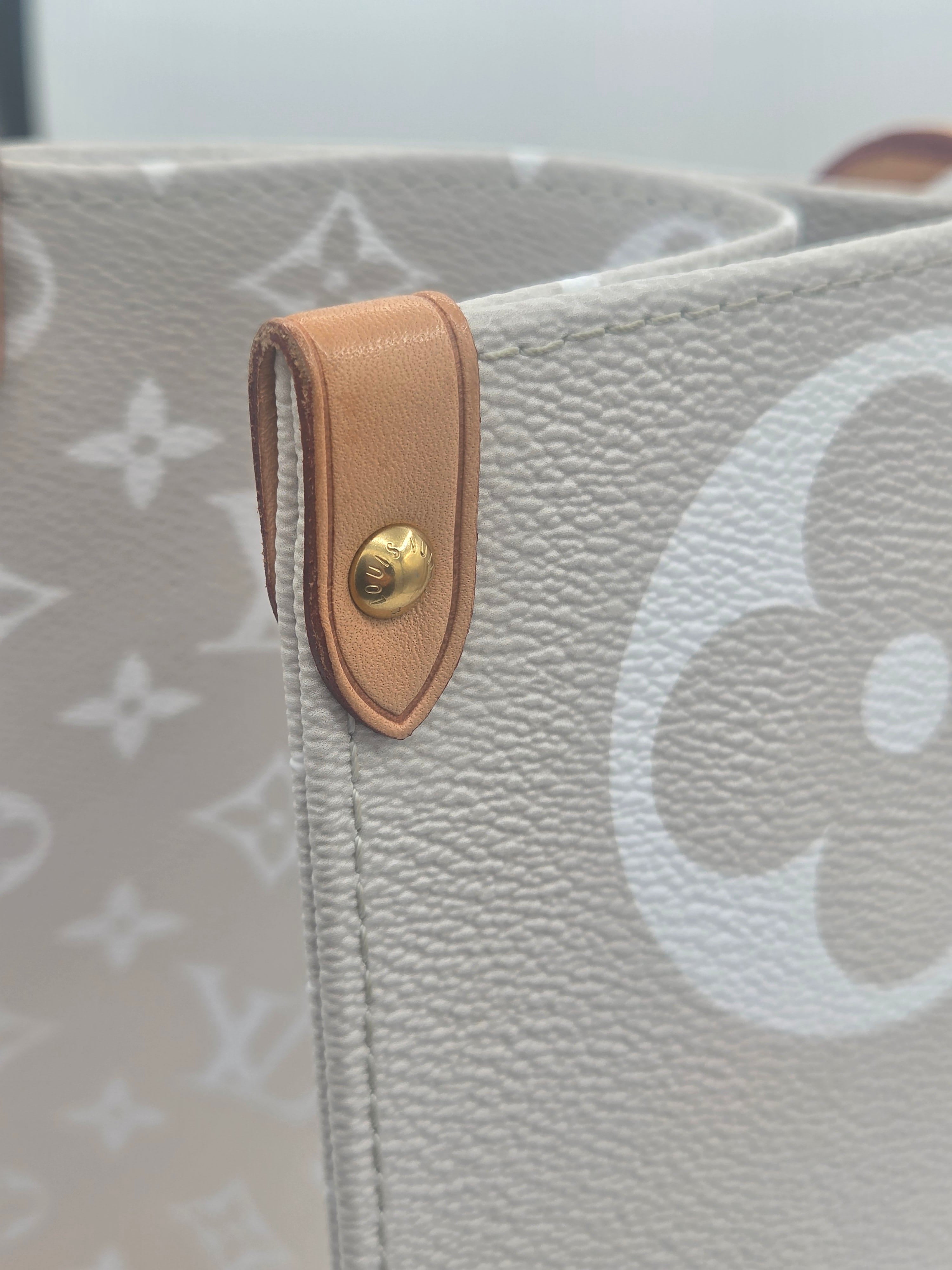 Close-up of a gray handbag with a brown leather strap and gold button.