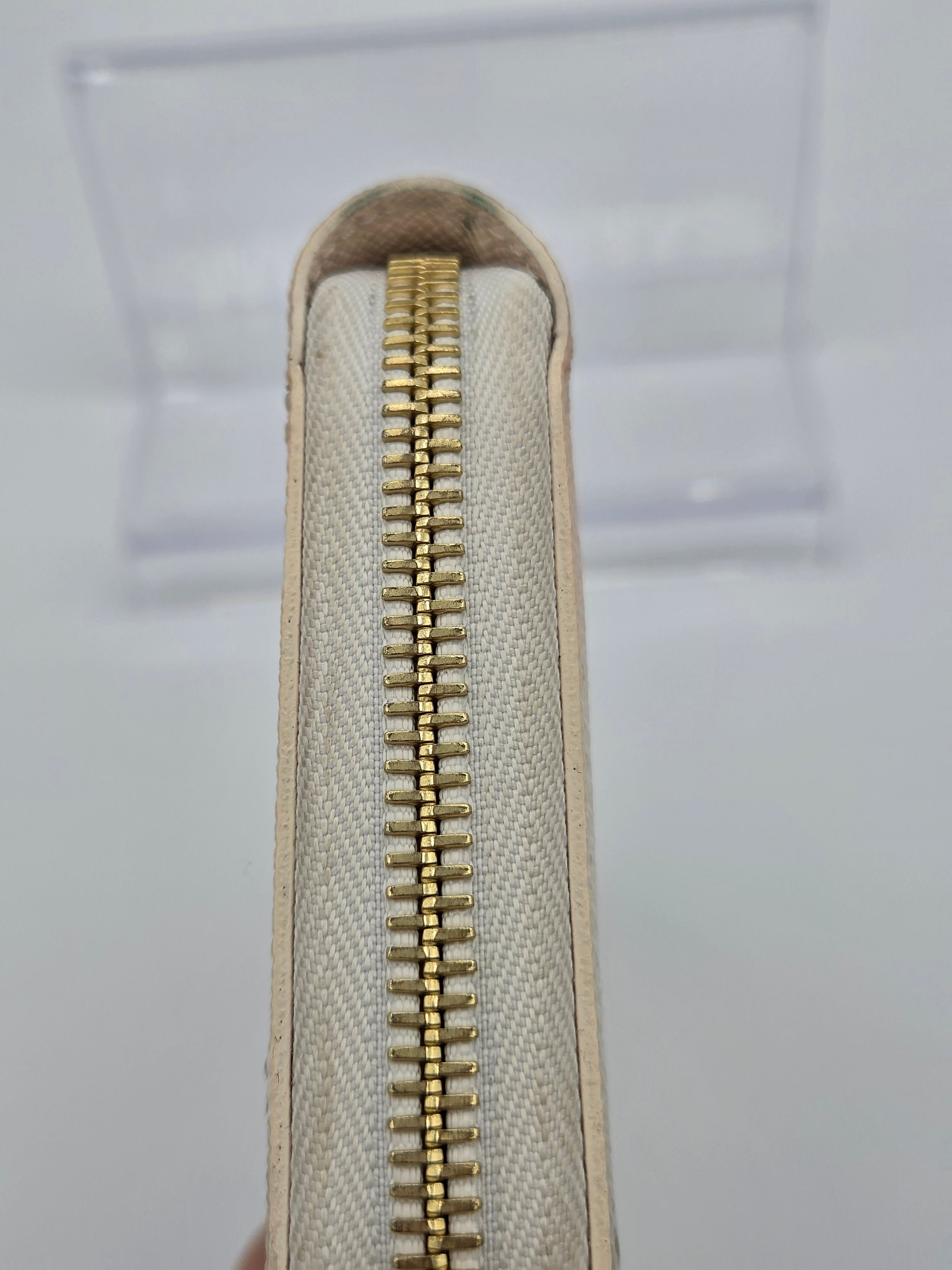 Close-up of a beige fabric pouch with a gold zipper on a light gray background