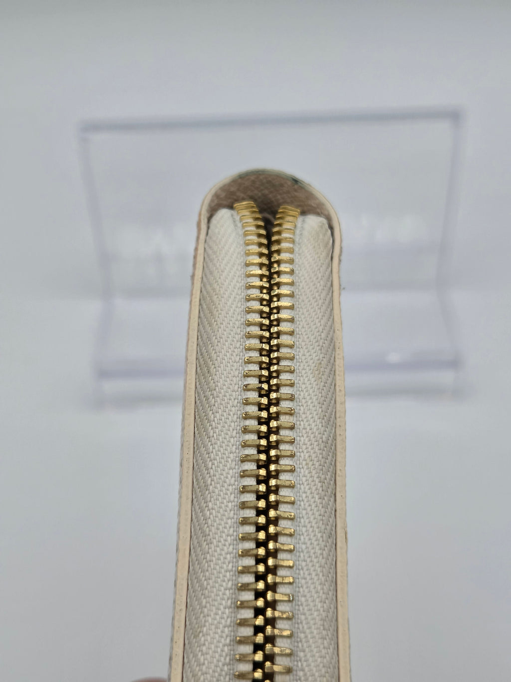Close-up of a beige clutch with a gold zipper on a light gray background