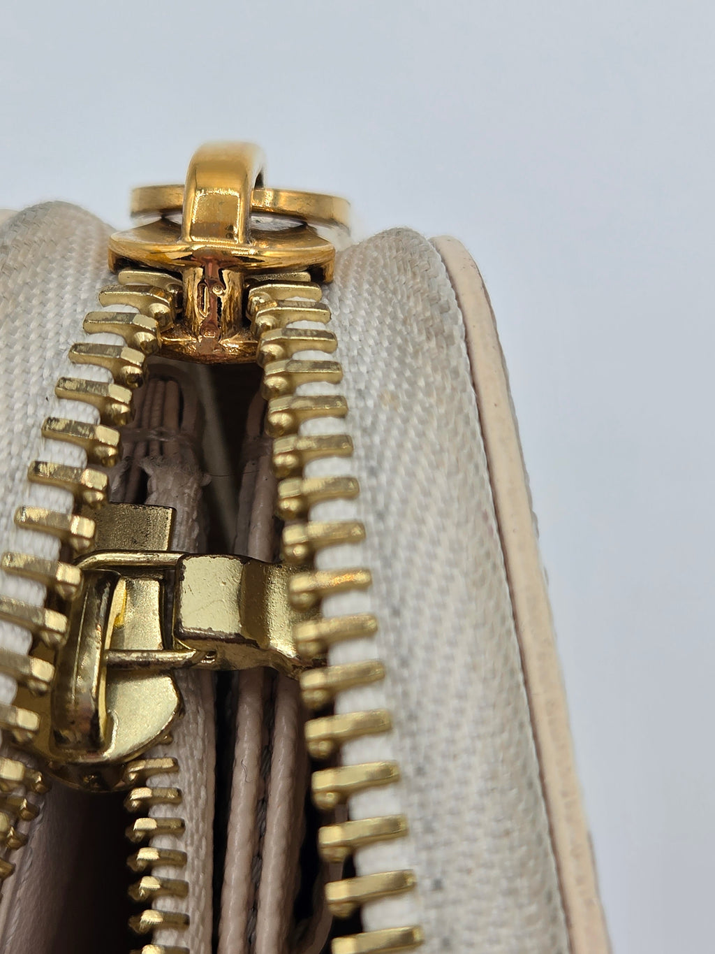 Close-up of a beige fabric pouch with a gold zipper on a light gray background