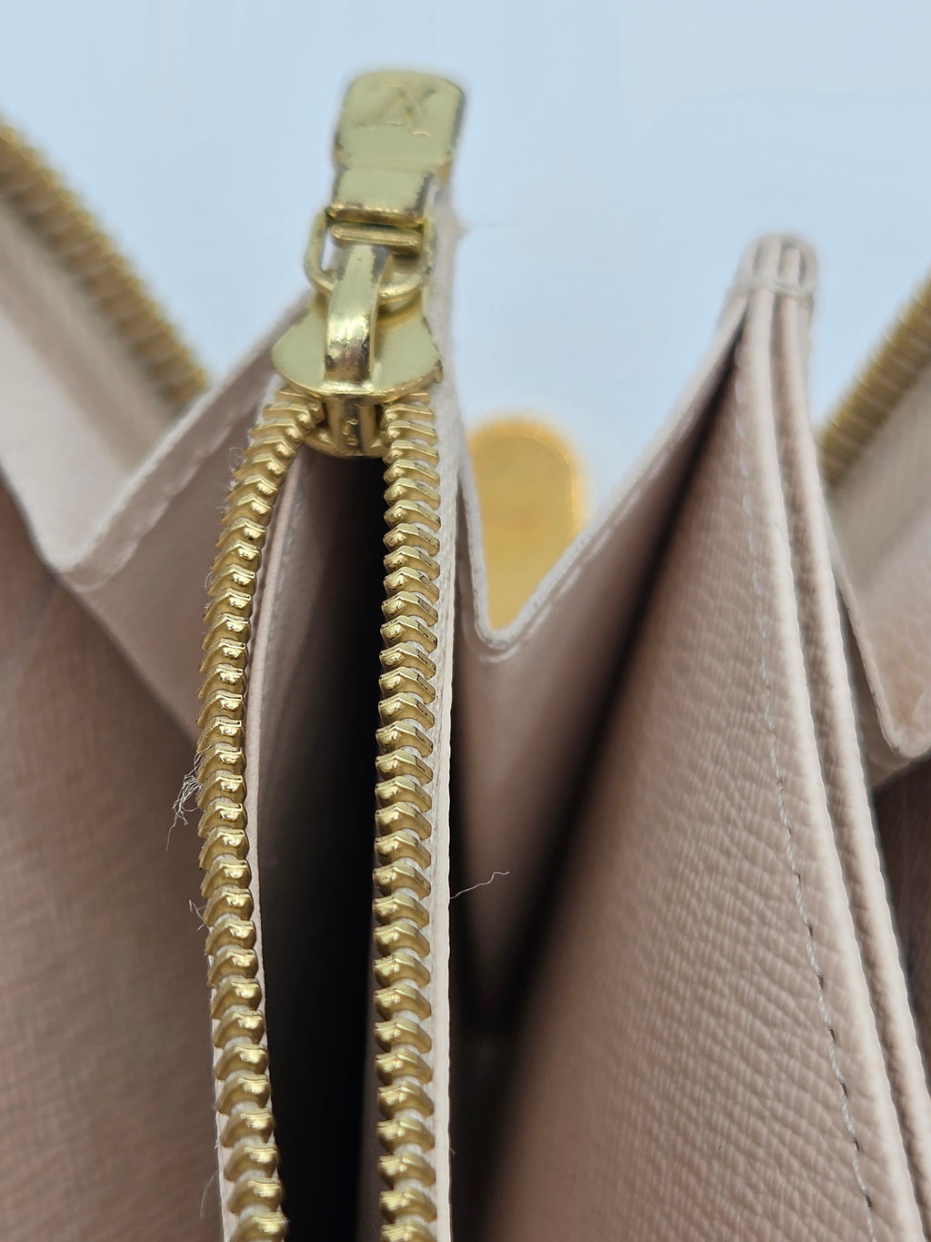 Close-up of a beige handbag with a gold zipper on a light blue background