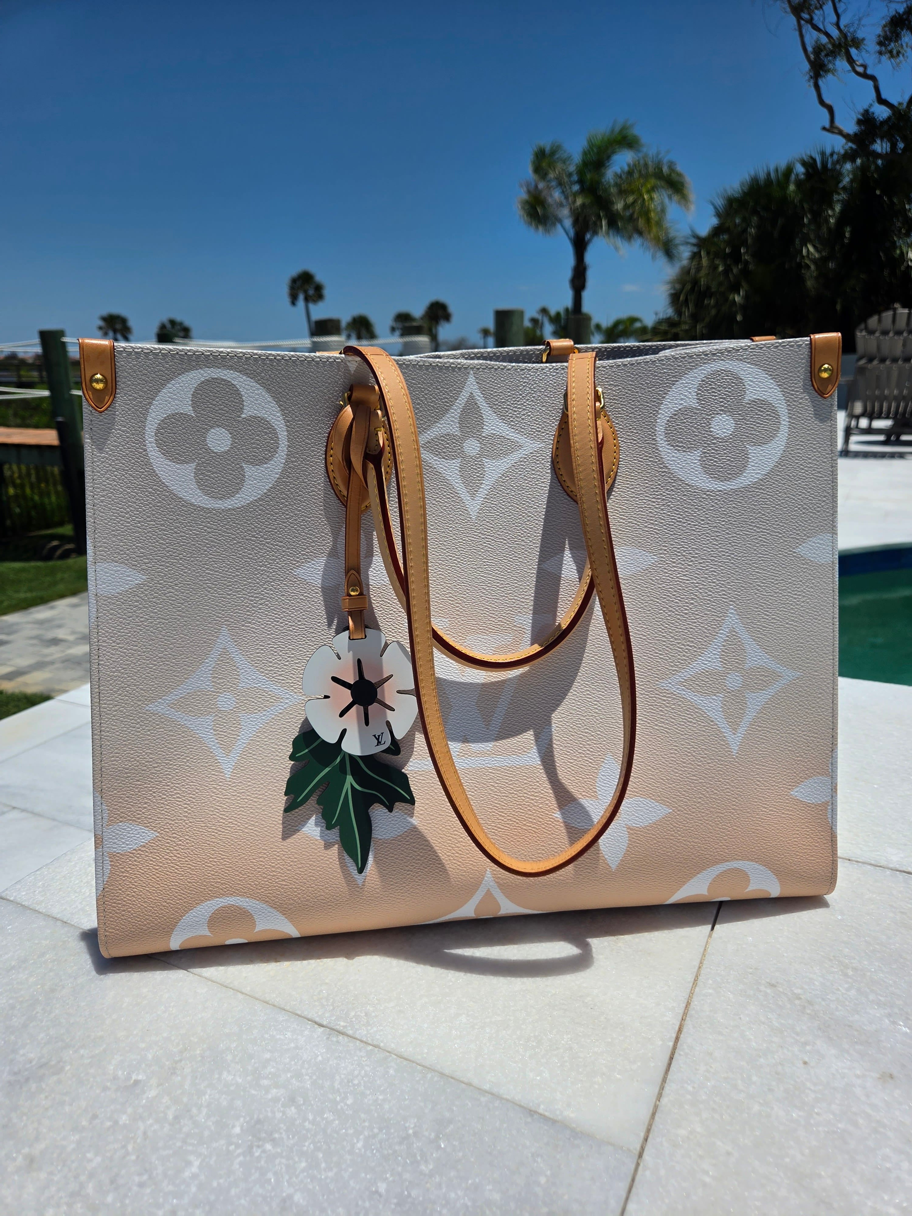 Designer handbag with floral pattern on a pavement with palm trees in the background