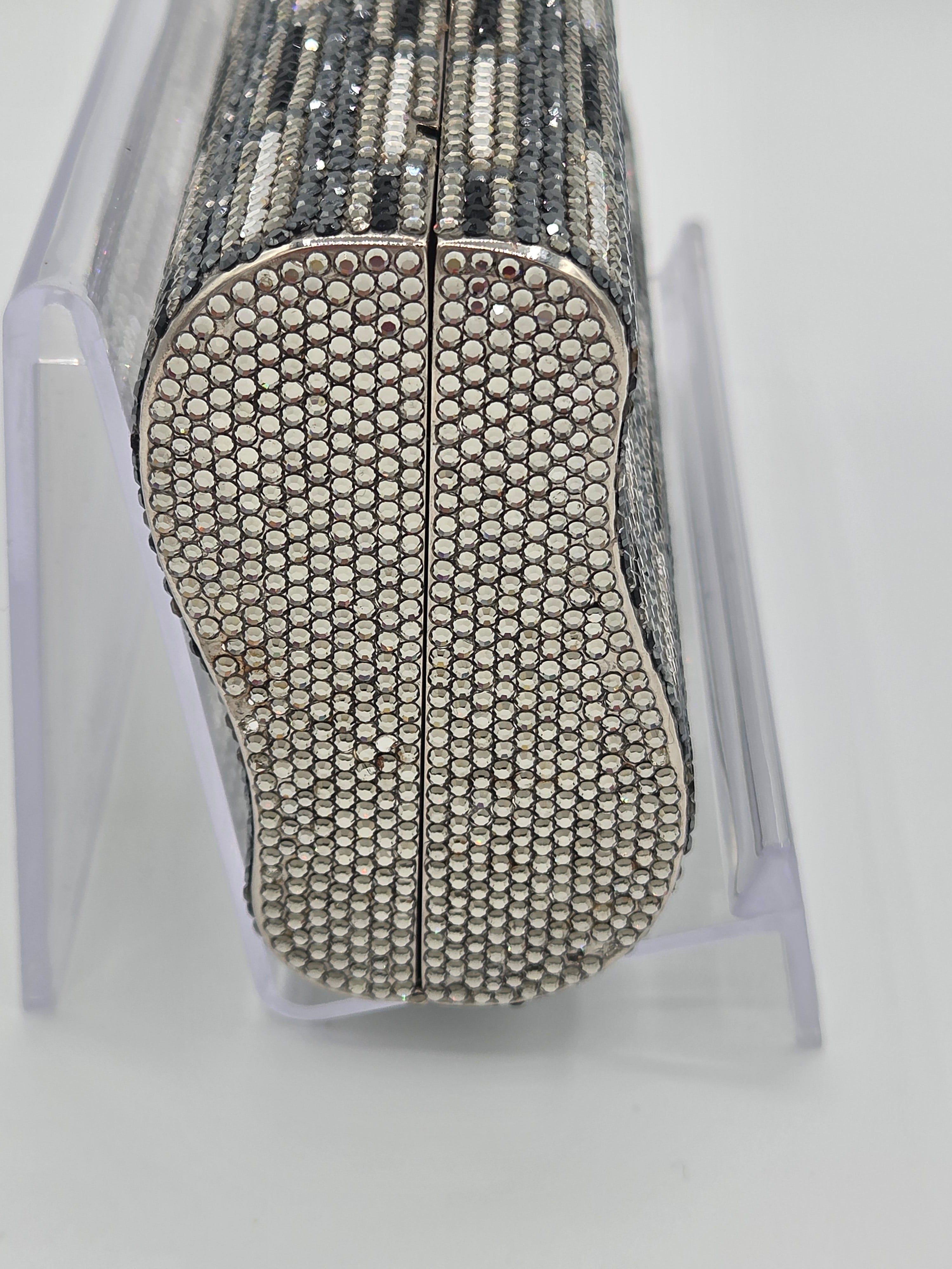 Silver clutch bag with rhinestone embellishments on a white stand