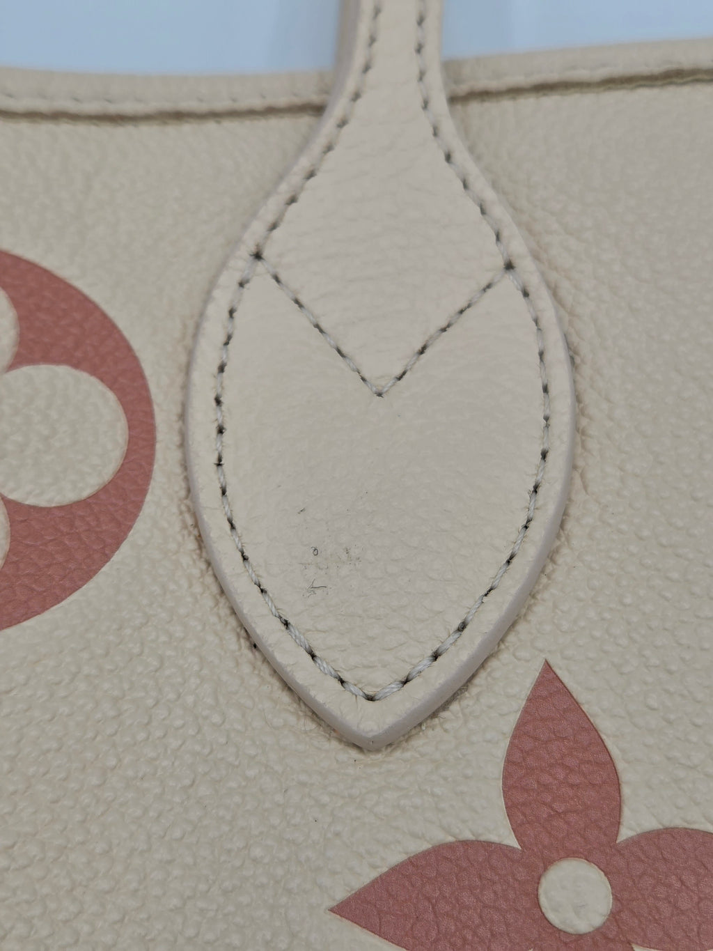 Close-up of a beige handbag with red floral design and visible brand logo.