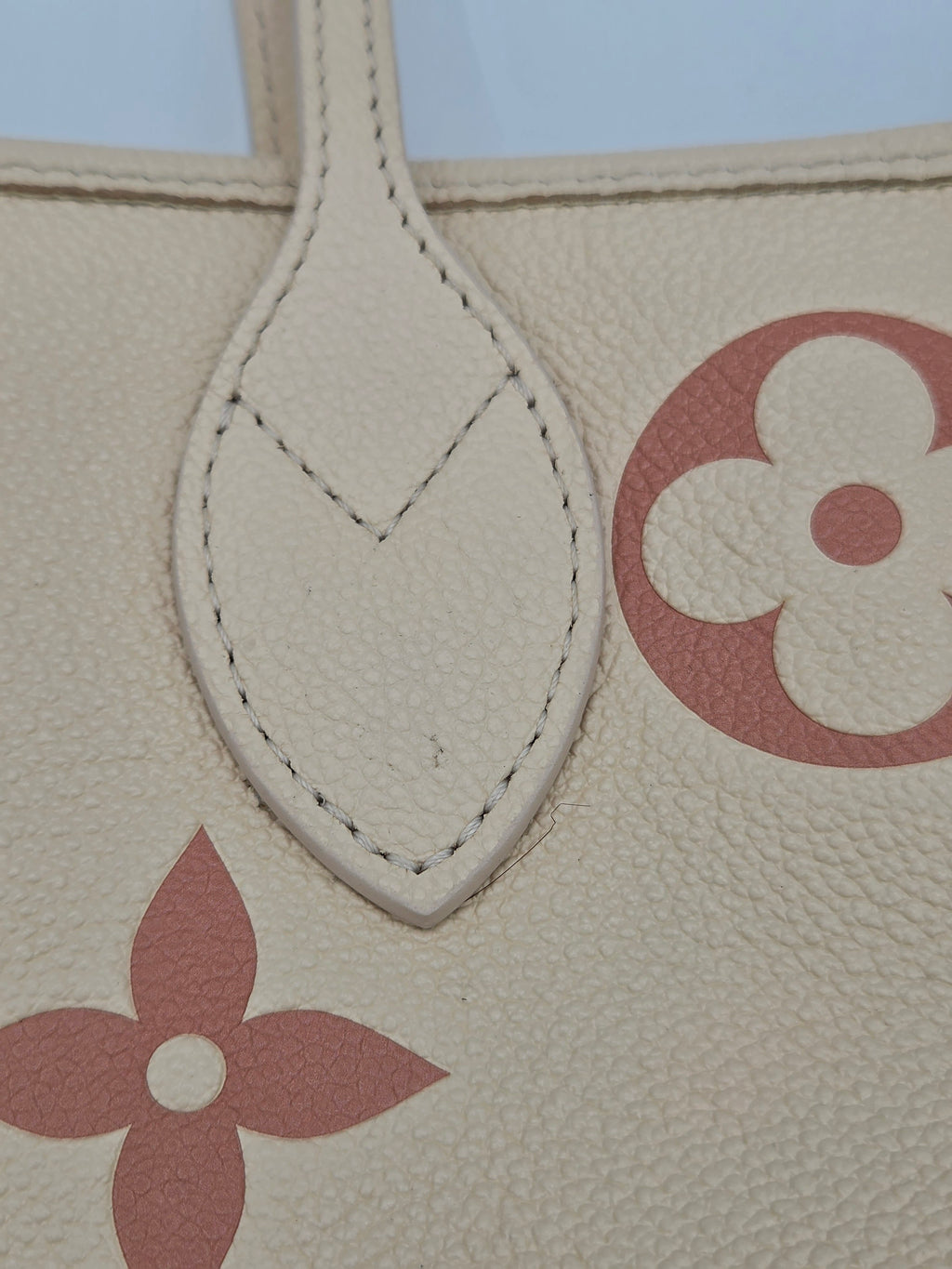 Close-up of a beige handbag with red floral designs on a light blue background