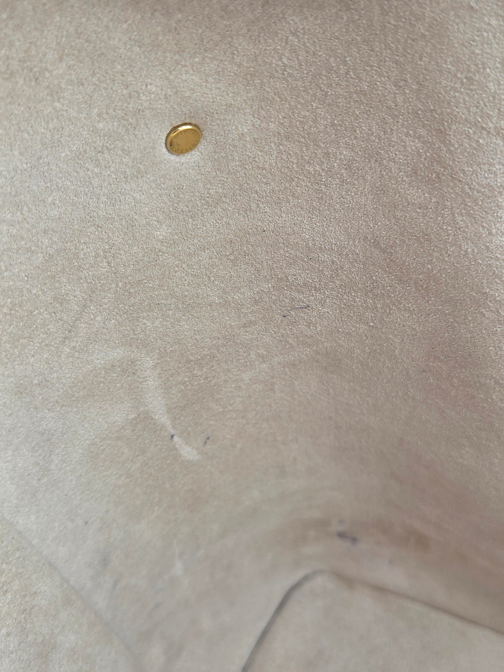 Close-up of a beige fabric surface with a gold button and visible thread.