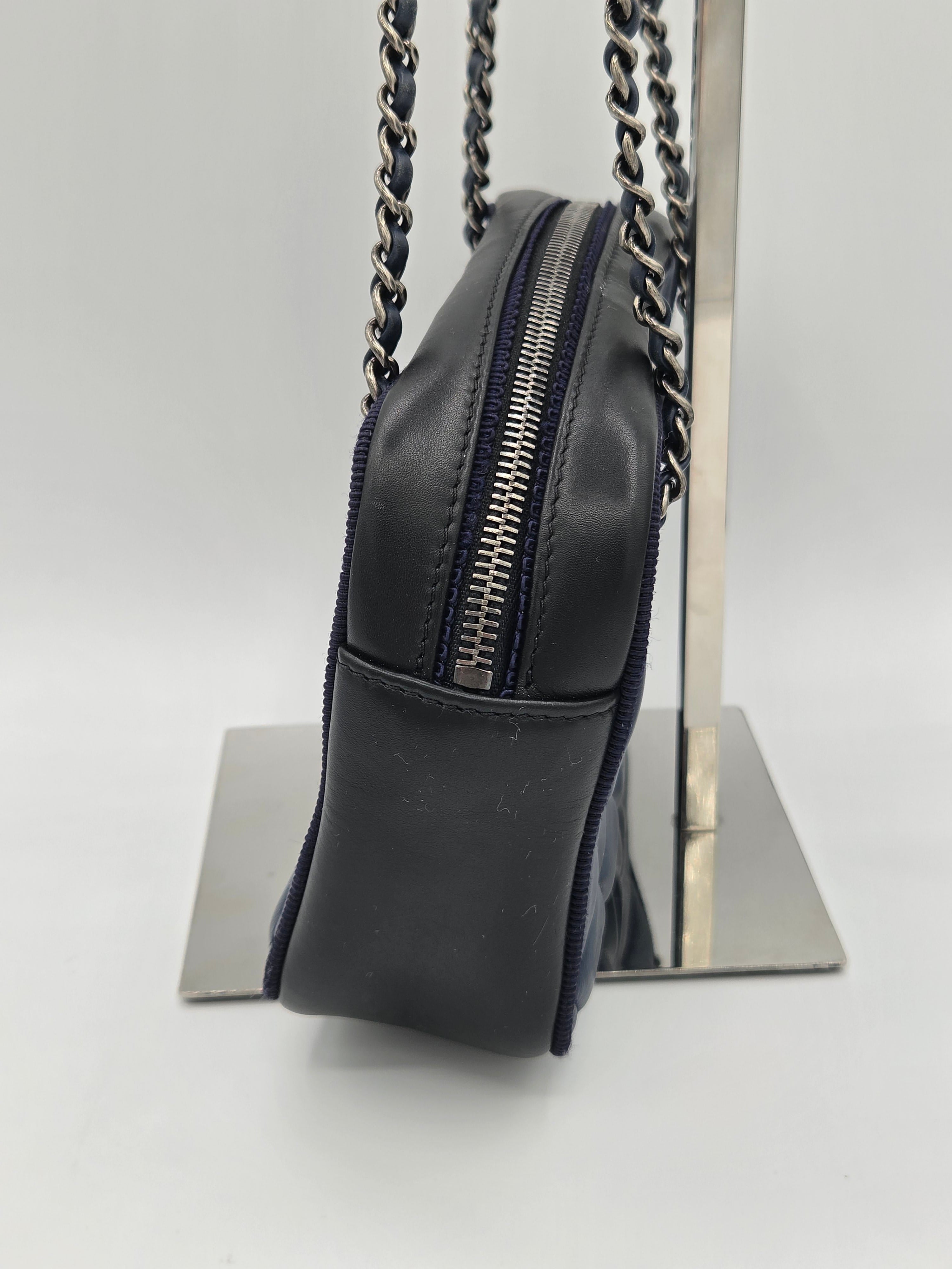 Black leather handbag with chain detail on a reflective surface