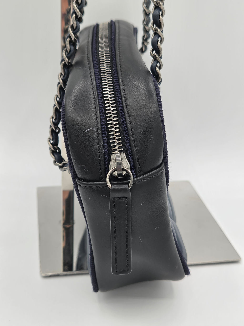 Black leather handbag with chain detail on a reflective surface