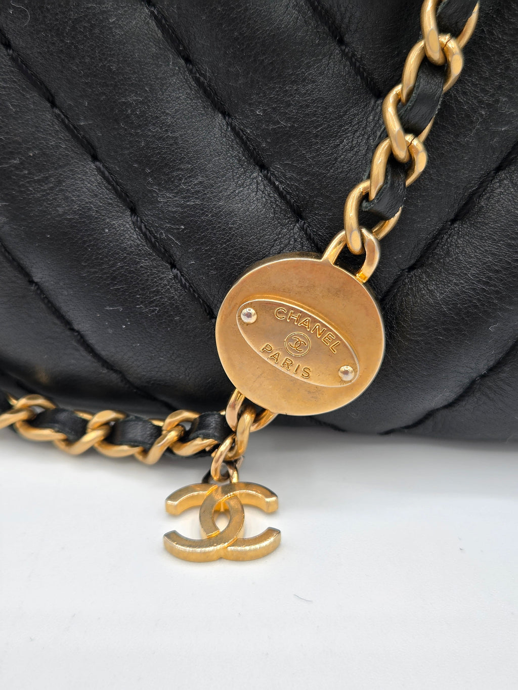 Gold chain with a round tag on a black quilted surface