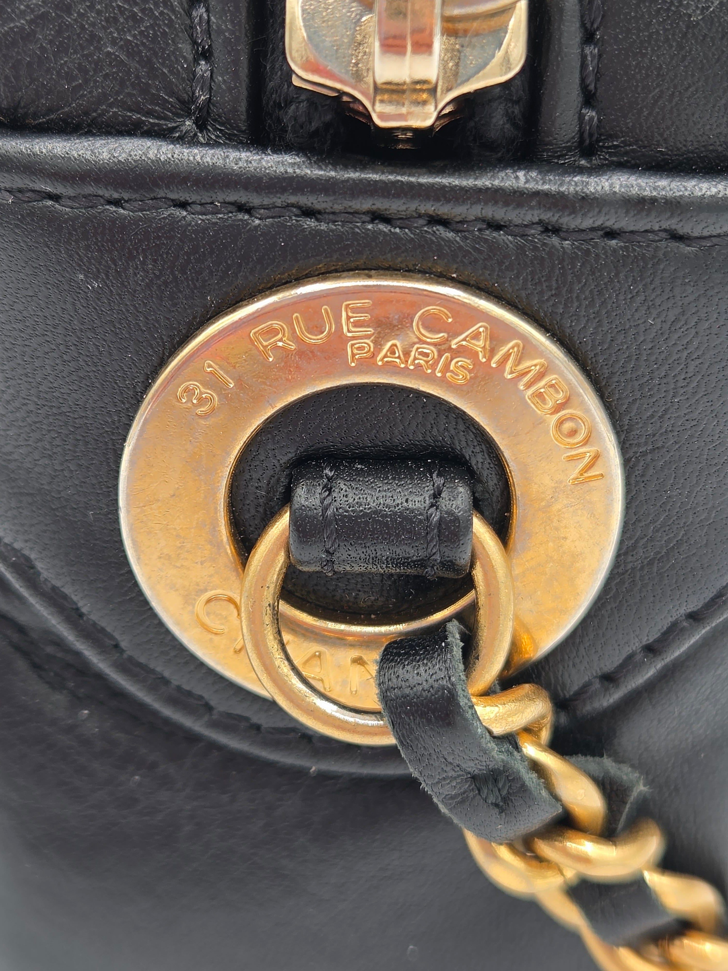 Close-up of a black handbag with gold hardware and 'Rue Cambon' logo.