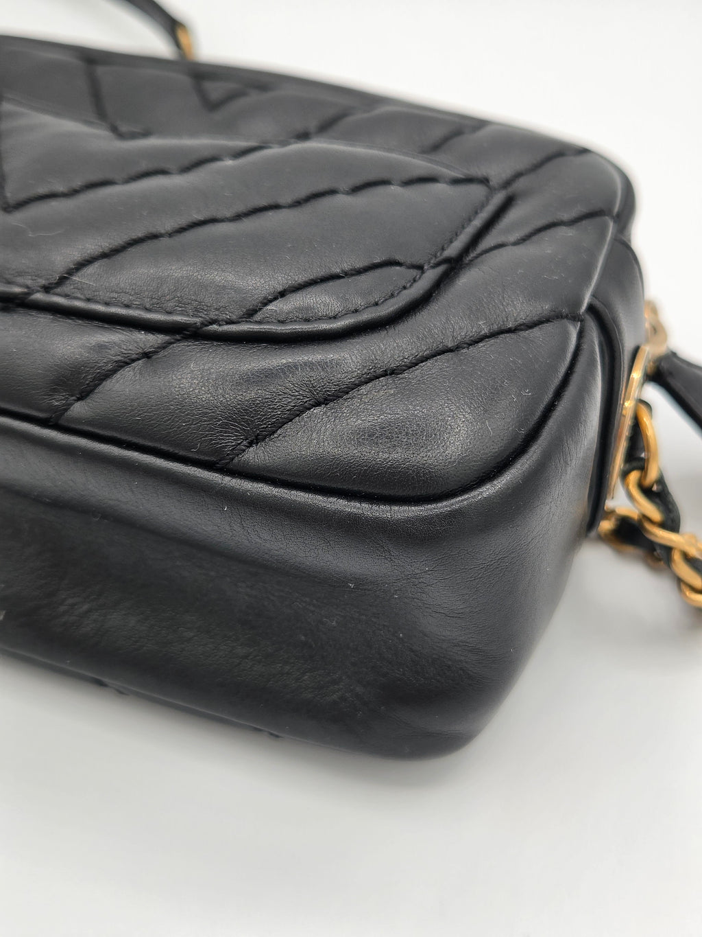 Black quilted handbag with gold chain strap on a light gray background
