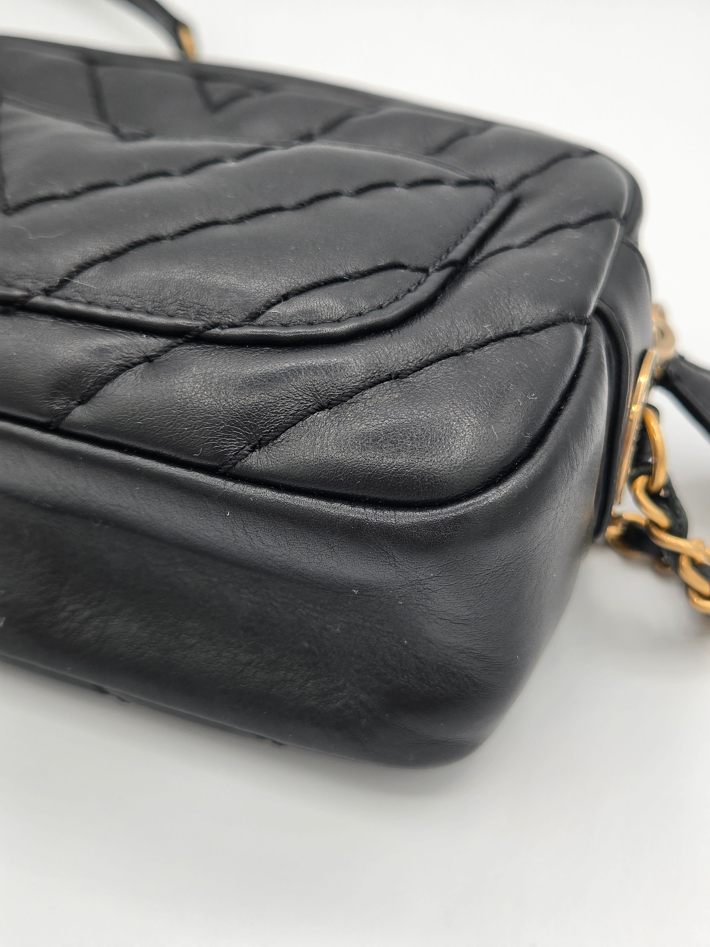 Black quilted handbag with gold chain strap on a light gray background