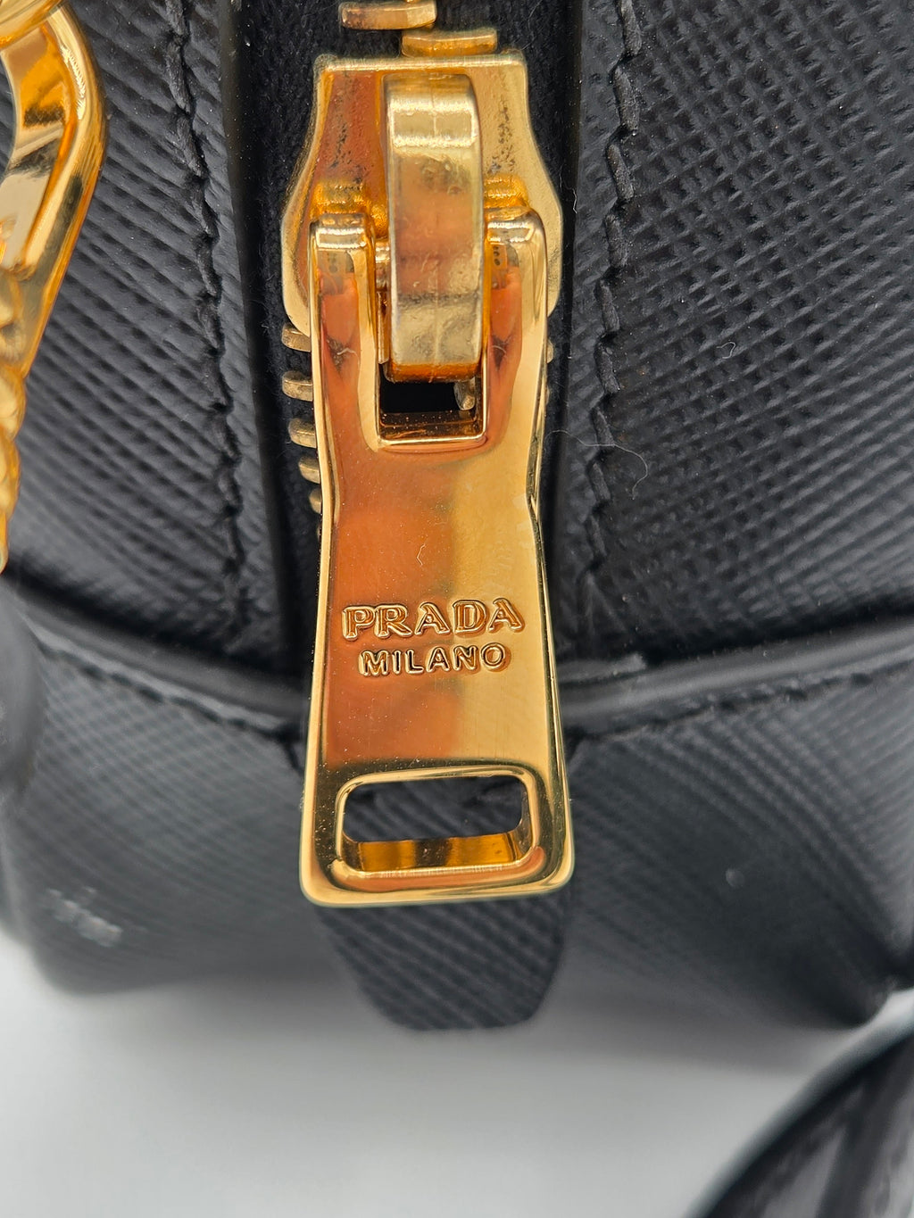 Close-up of a Prada handbag with gold hardware on a black textured background