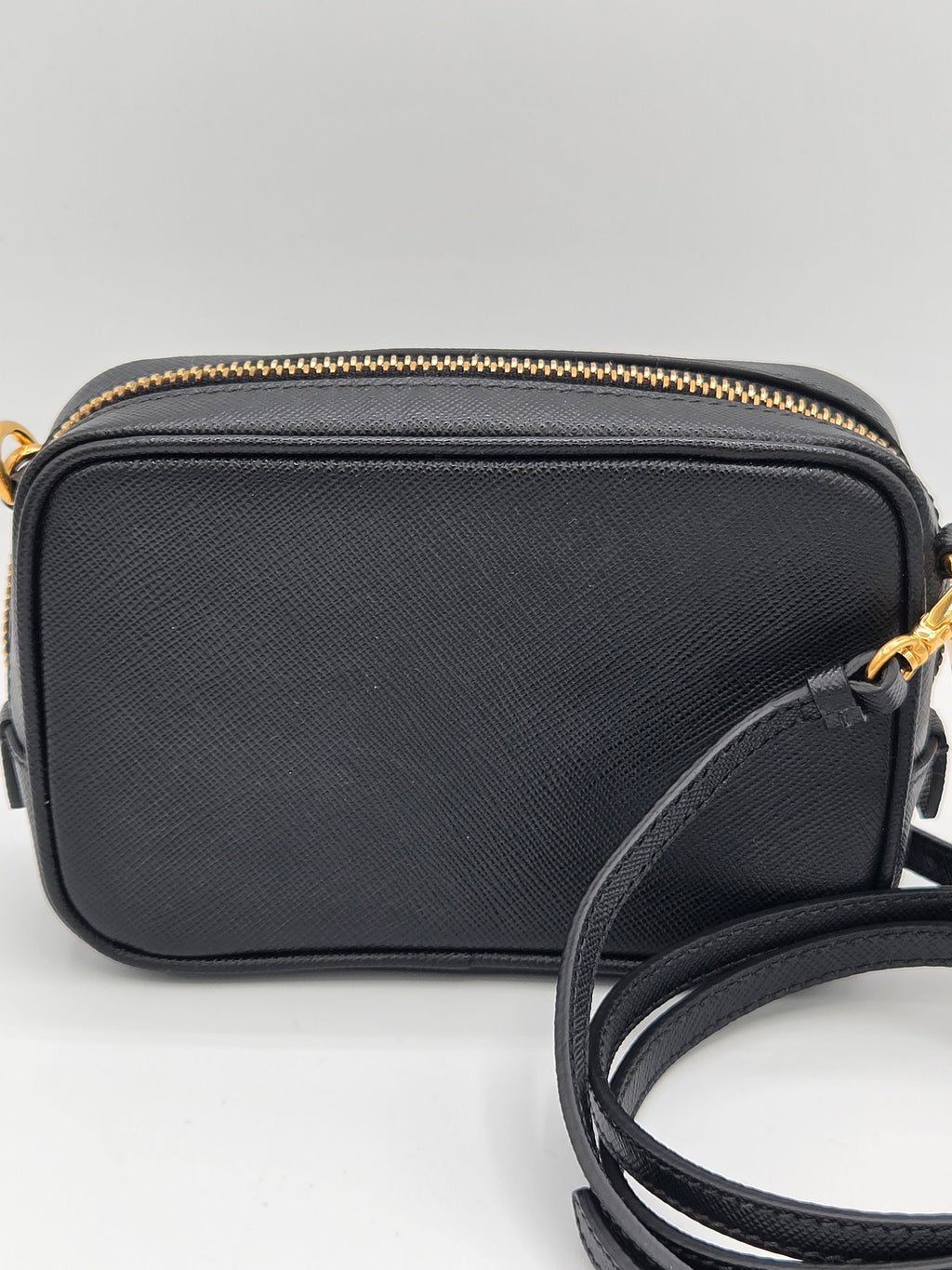 Black crossbody bag with a strap on a light gray background