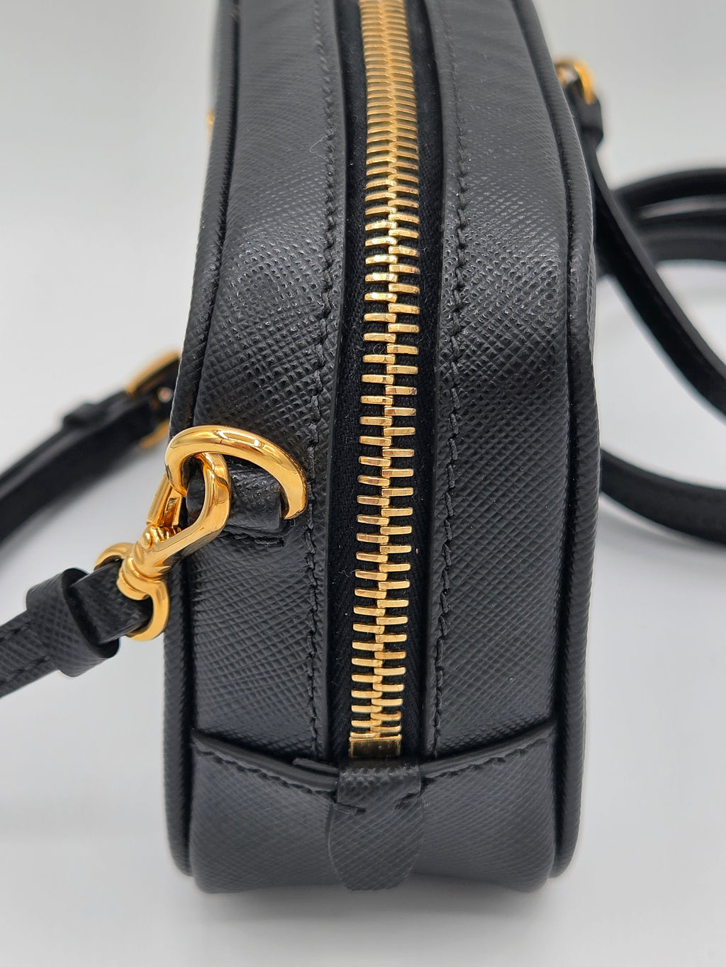 Black handbag with gold zipper and handle on a light gray background