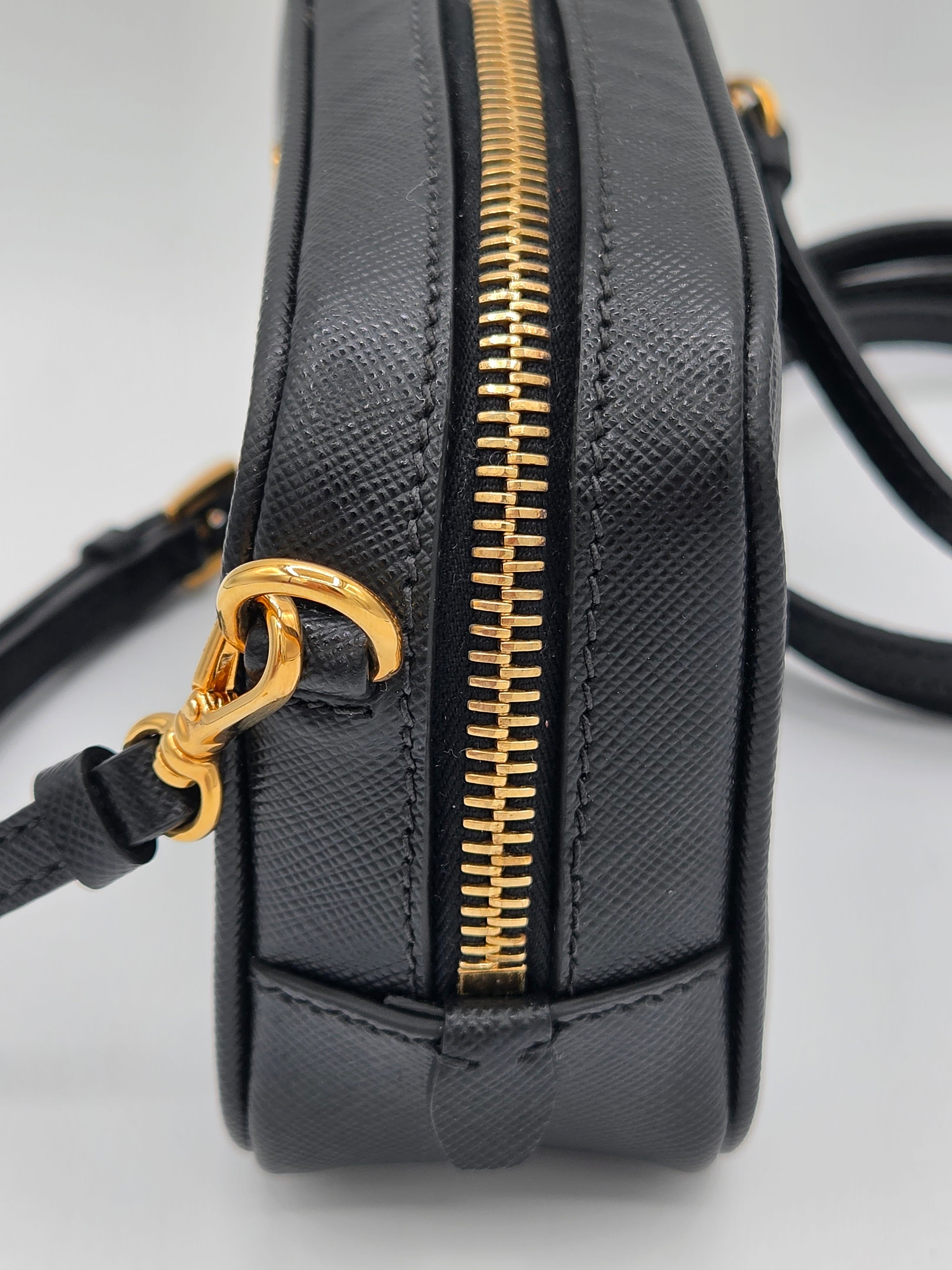 Black handbag with gold zipper and handle on a light gray background