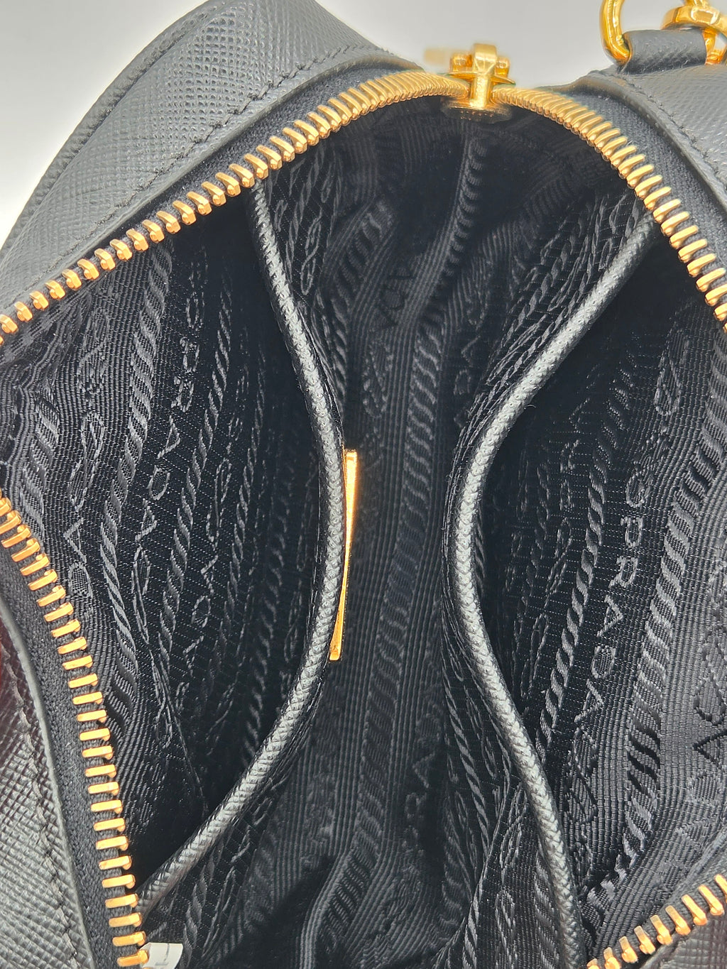 Close-up of a Prada handbag with gold zipper and Prada branding.