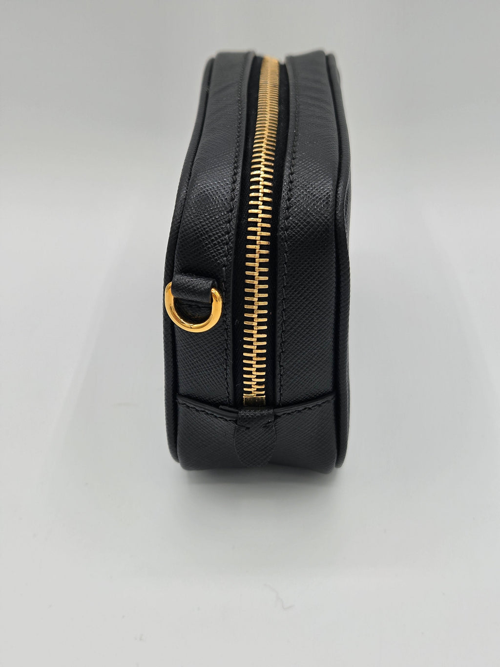 Black belt bag with gold zipper and buckle on a light gray background
