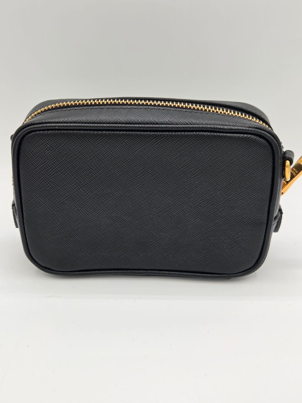 Black rectangular pouch with gold zipper on a light gray background