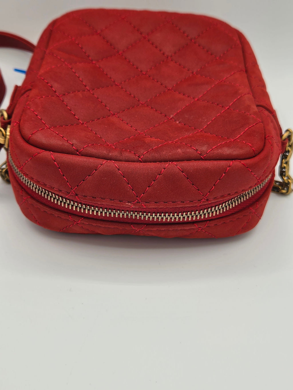 Red quilted handbag with a gold zipper on a light gray background